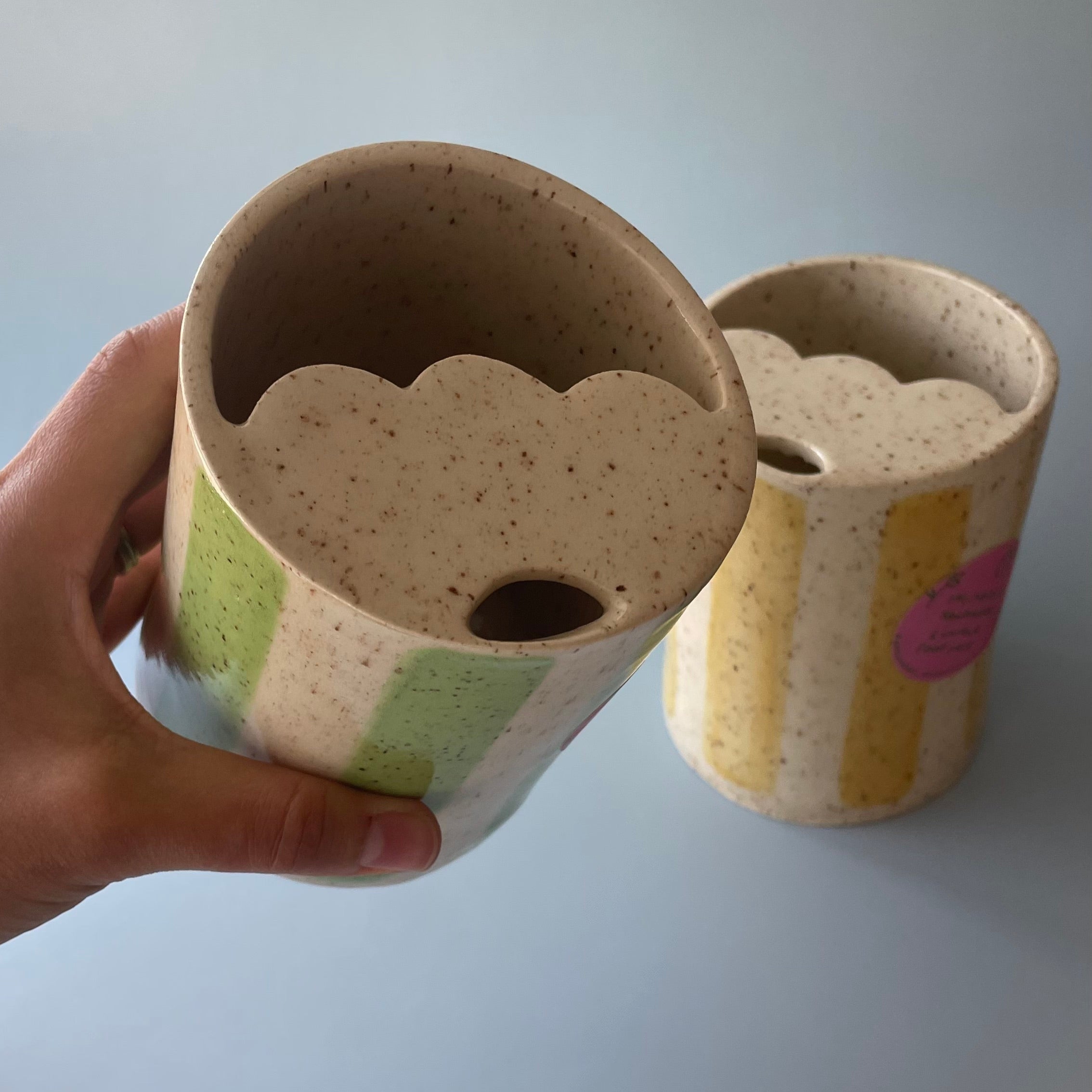 travel mugs with a scalloped lid, and sip hole, glazed with a beige base with brown speckles and comes in either yellow or green striped detail