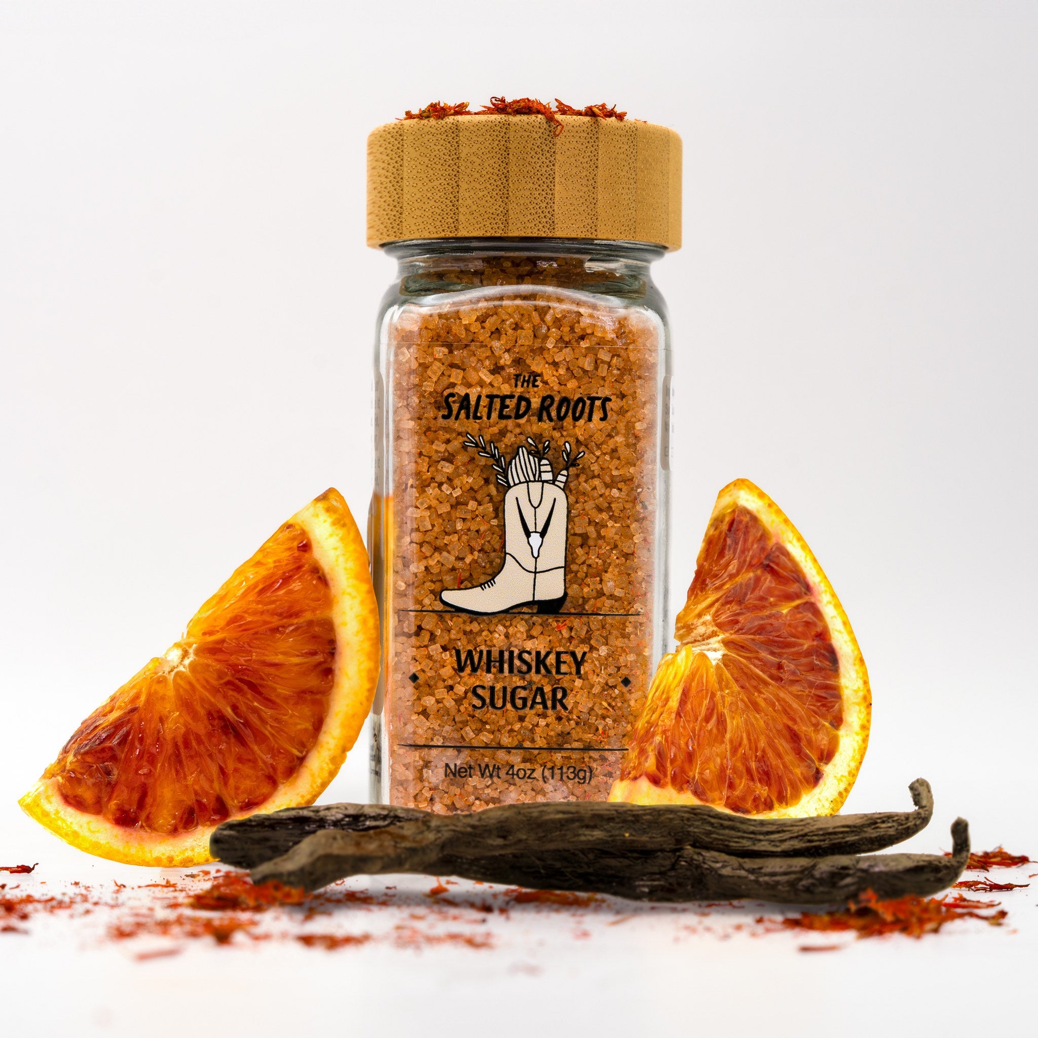 Glass salt jar with wooden lid and labels. Surrounded by orange slices, vanilla bean, and safflower.