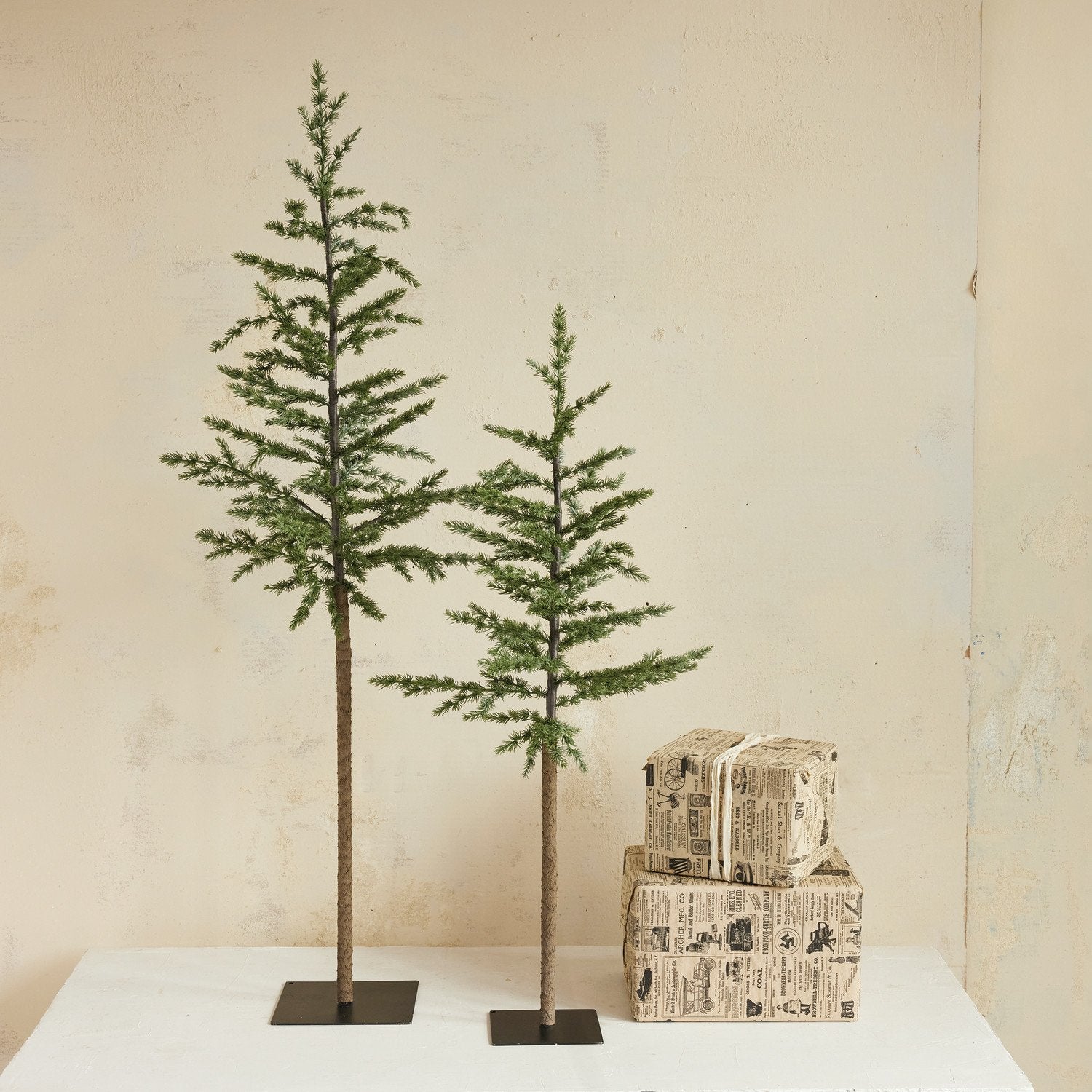 Two artificial trees on stands with stacked boxes against a beige wall.