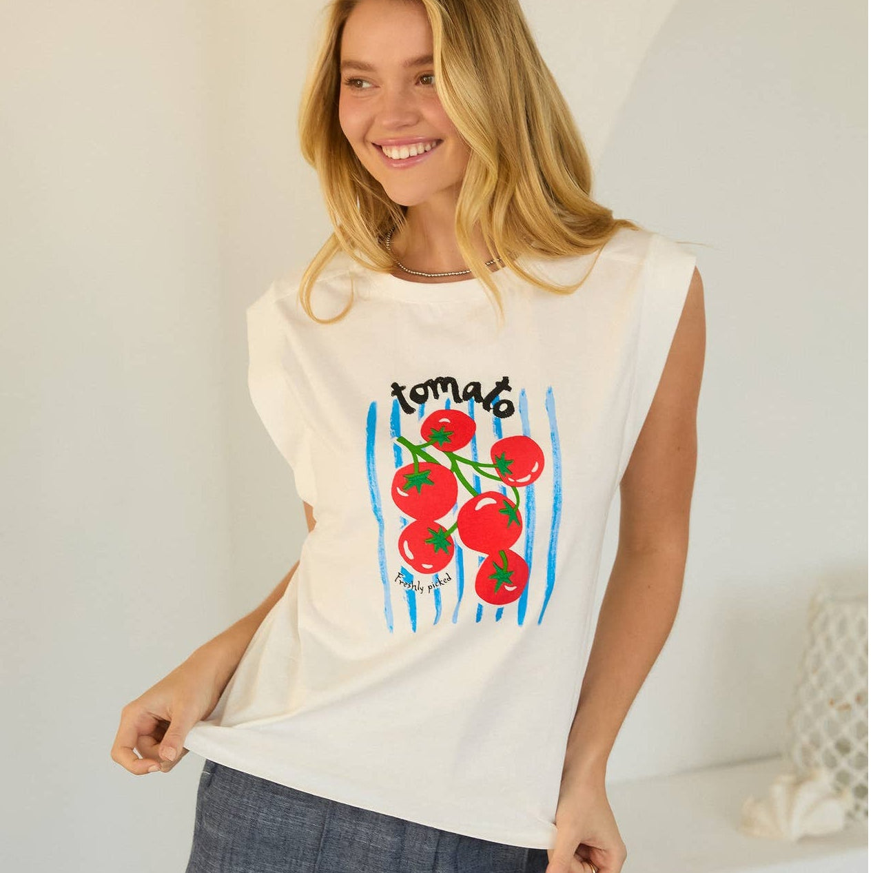 Woman wearing a sleeveless top with tomato design and denim shorts indoors.