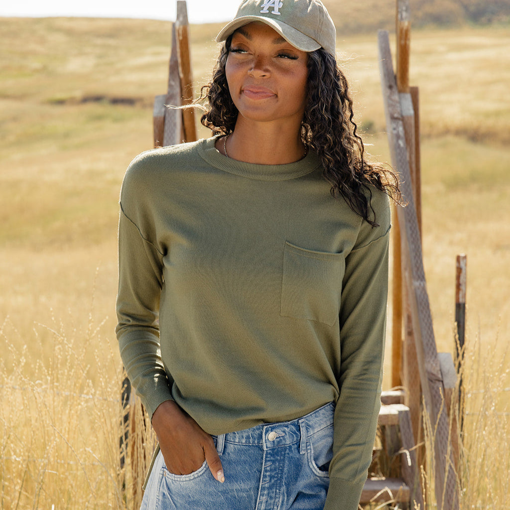 Featuring a playful high-low hemline and whimsical side slits, this sweater is as stylish as it is comfy! With ribbed details, a patch pocket, and a relaxed boxy fit, you'll feel warm and wonderful all day long. Olive Drab