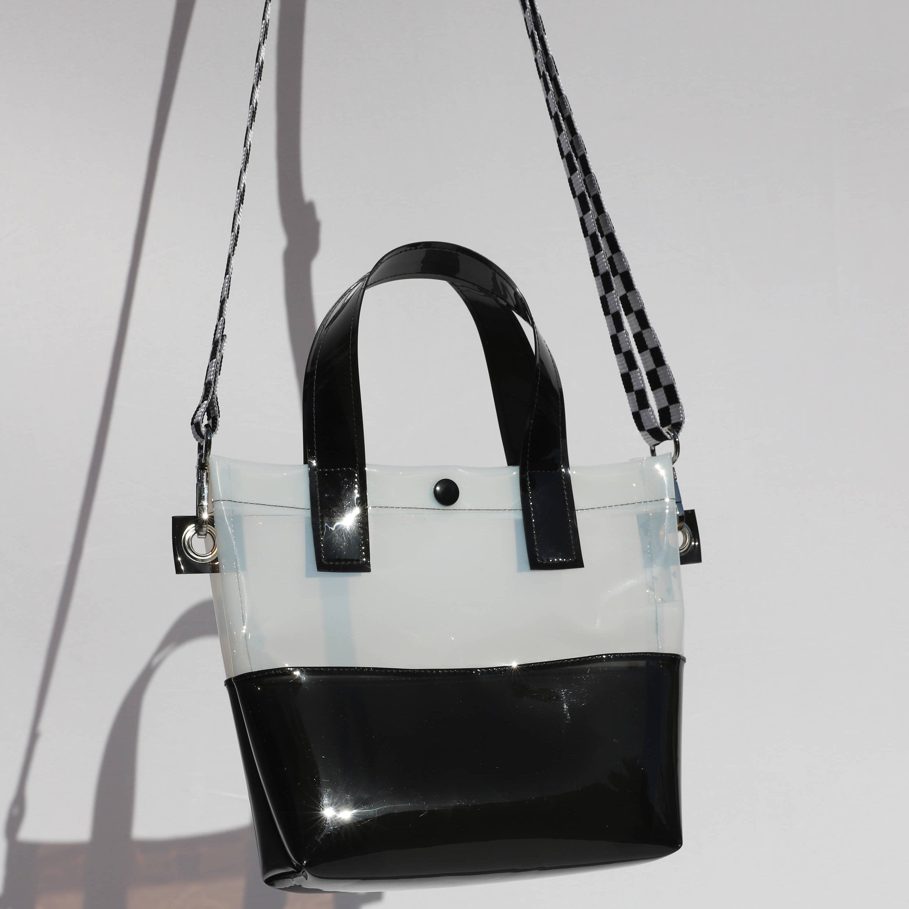 Miss your jelly sandals? This is your new favorite bag! Keep everything inside with a snap. The black and white translucent vinyl handle bag has a black snap closure and is detailed with silver metal grommets. It's available with or without the detachable black and white checkered 1" strap
