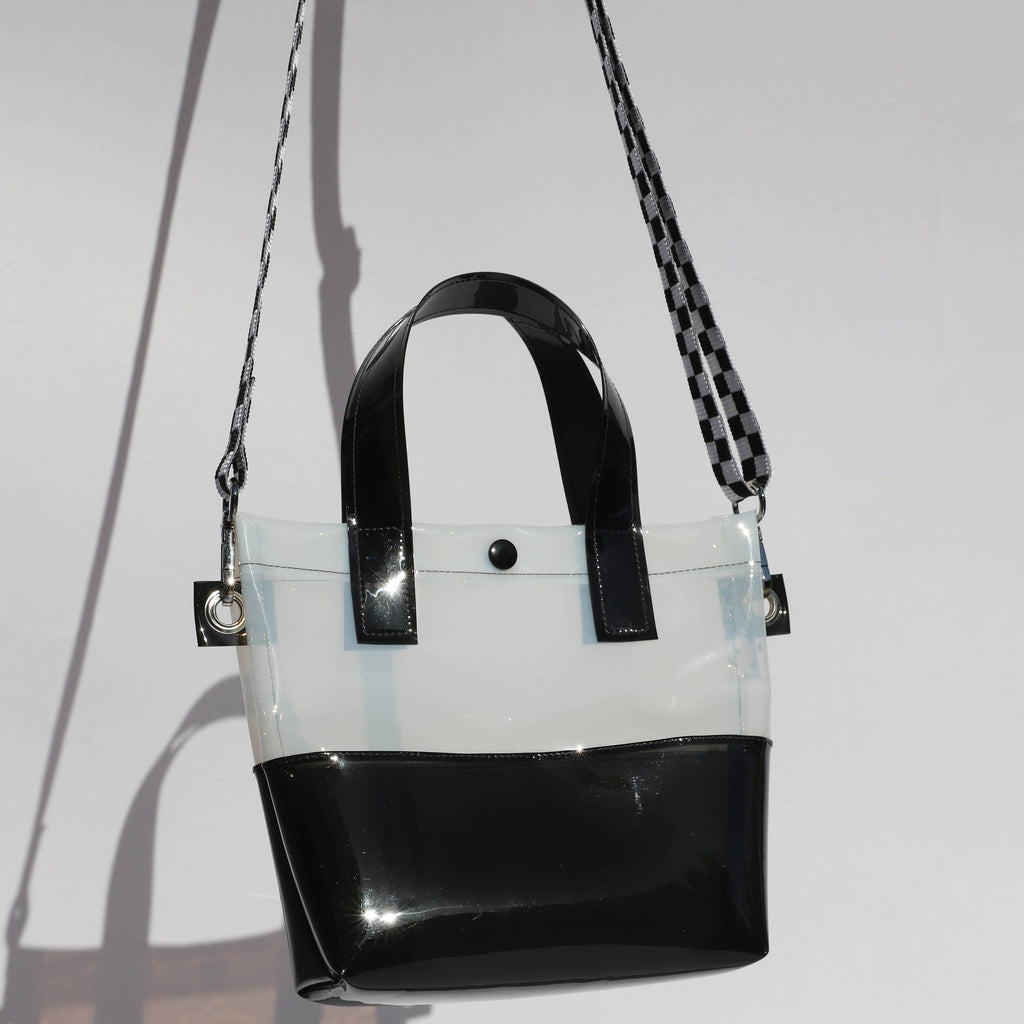 Miss your jelly sandals? This is your new favorite bag! Keep everything inside with a snap. The black and white translucent vinyl handle bag has a black snap closure and is detailed with silver metal grommets. It's available with or without the detachable black and white checkered 1" strap