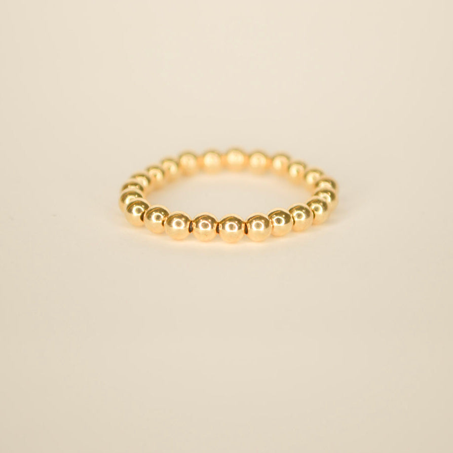 Gold beaded stretchable ring on an off white back ground.