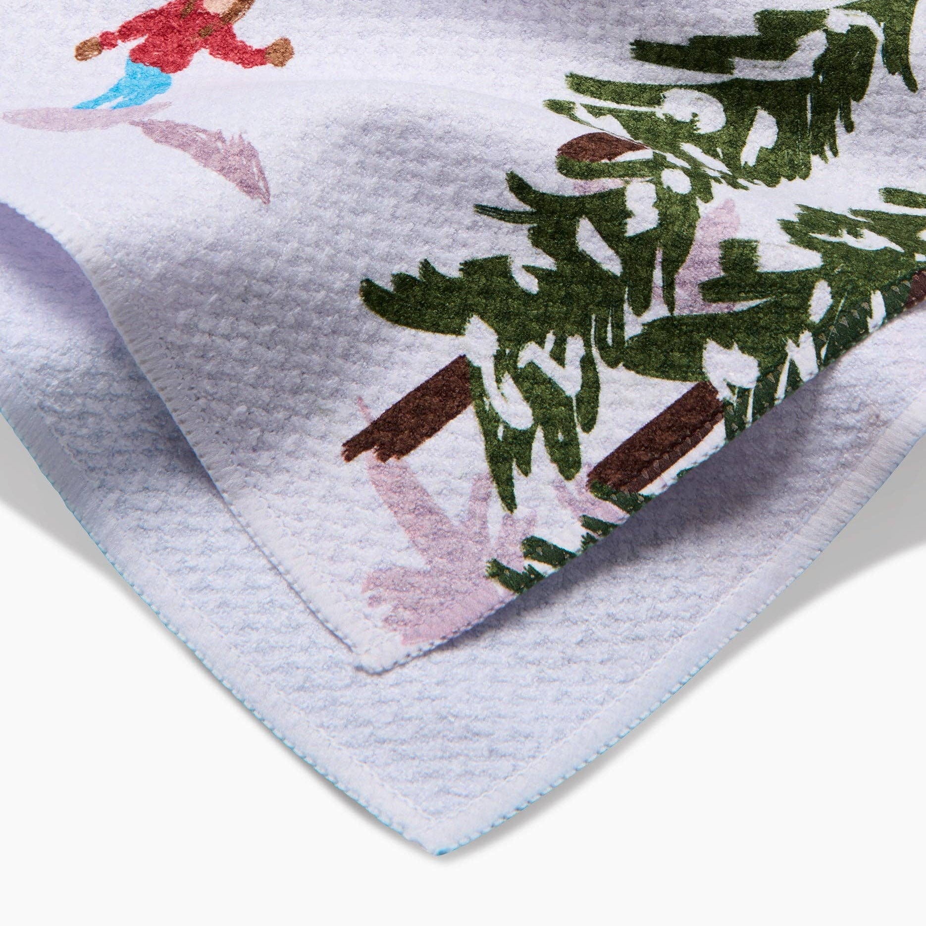 Tea towel with winter scene design featuring a child skiing and a Christmas tree.