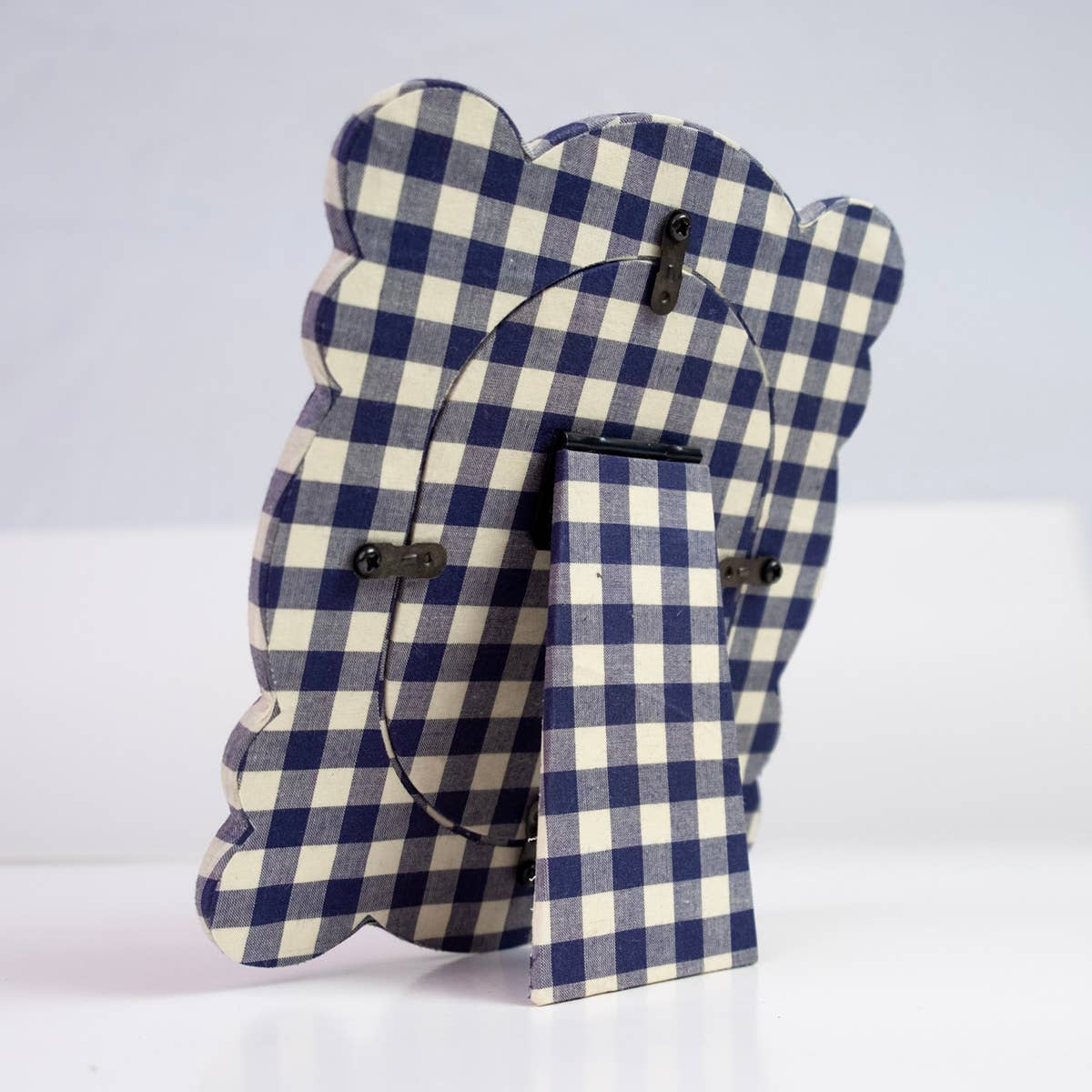 A decorative wooden picture frame with a blue and cream gingham checkered pattern, shown from the back on a white surface against a light gray background.