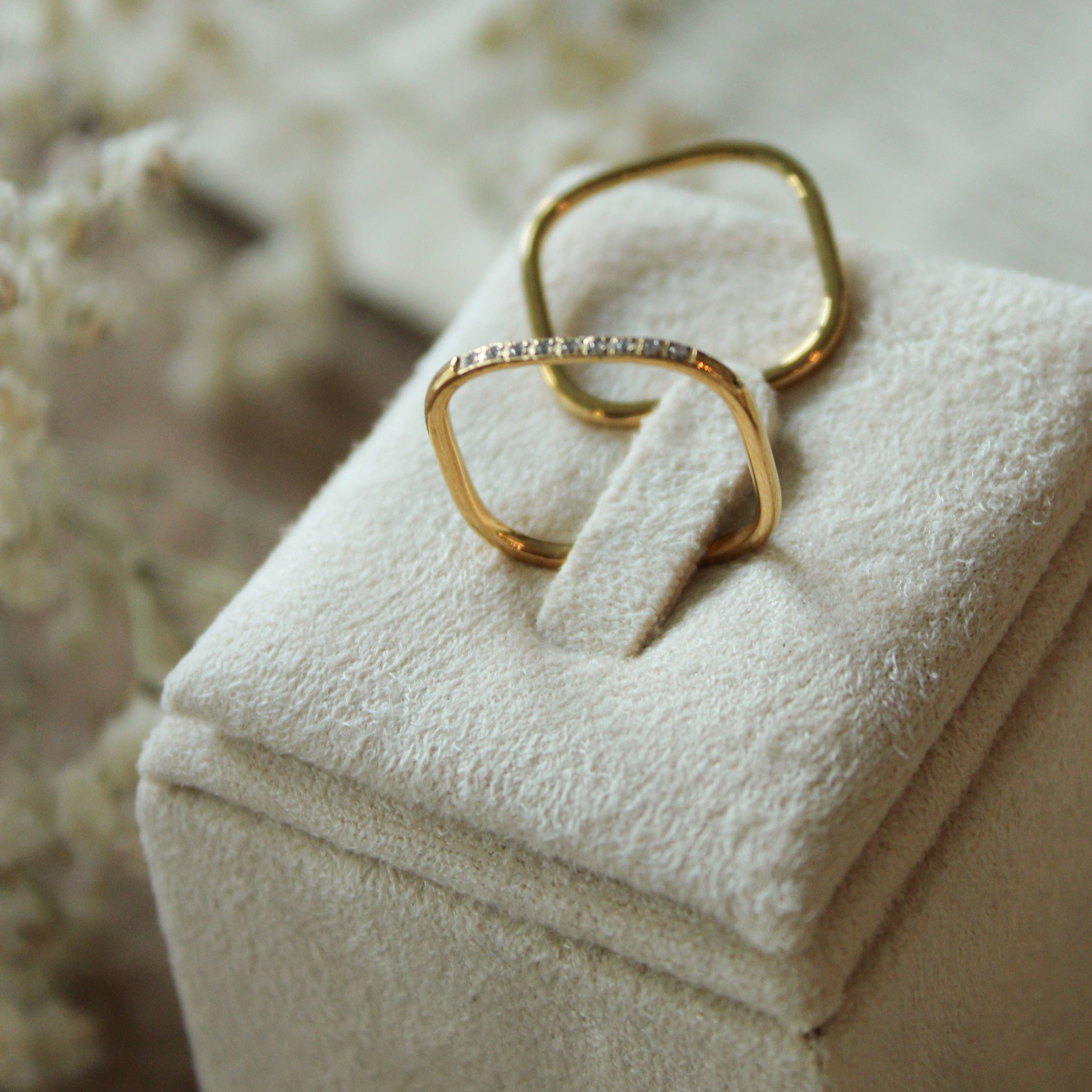Gold ring with a diamond on a white jewelry box with flowers in the background