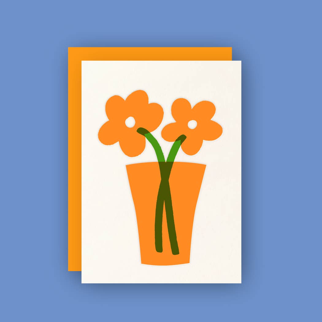 A white greeting card displays a simple illustration of two orange flowers with white centers and green stems in an orange vase. The card is placed on an orange envelope against a solid blue background.