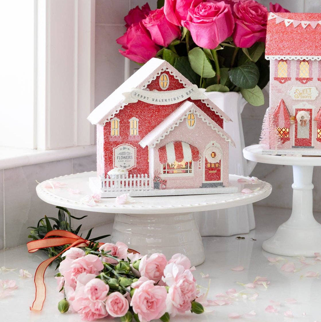 lluminate your Valentine village with this enchanting battery-operated Flower Shop! This charming paper house glows with warm, festive light, transforming any display into a magical romantic scene. Perfect for creating an interactive village experience, the built-in lighting adds ambiance and draws everyone's attention to this adorable floral boutique.

Details:

Red, pink, and cream valentine flower shop
Flower shop is 6" wide x 4.5" deep x 7" tall