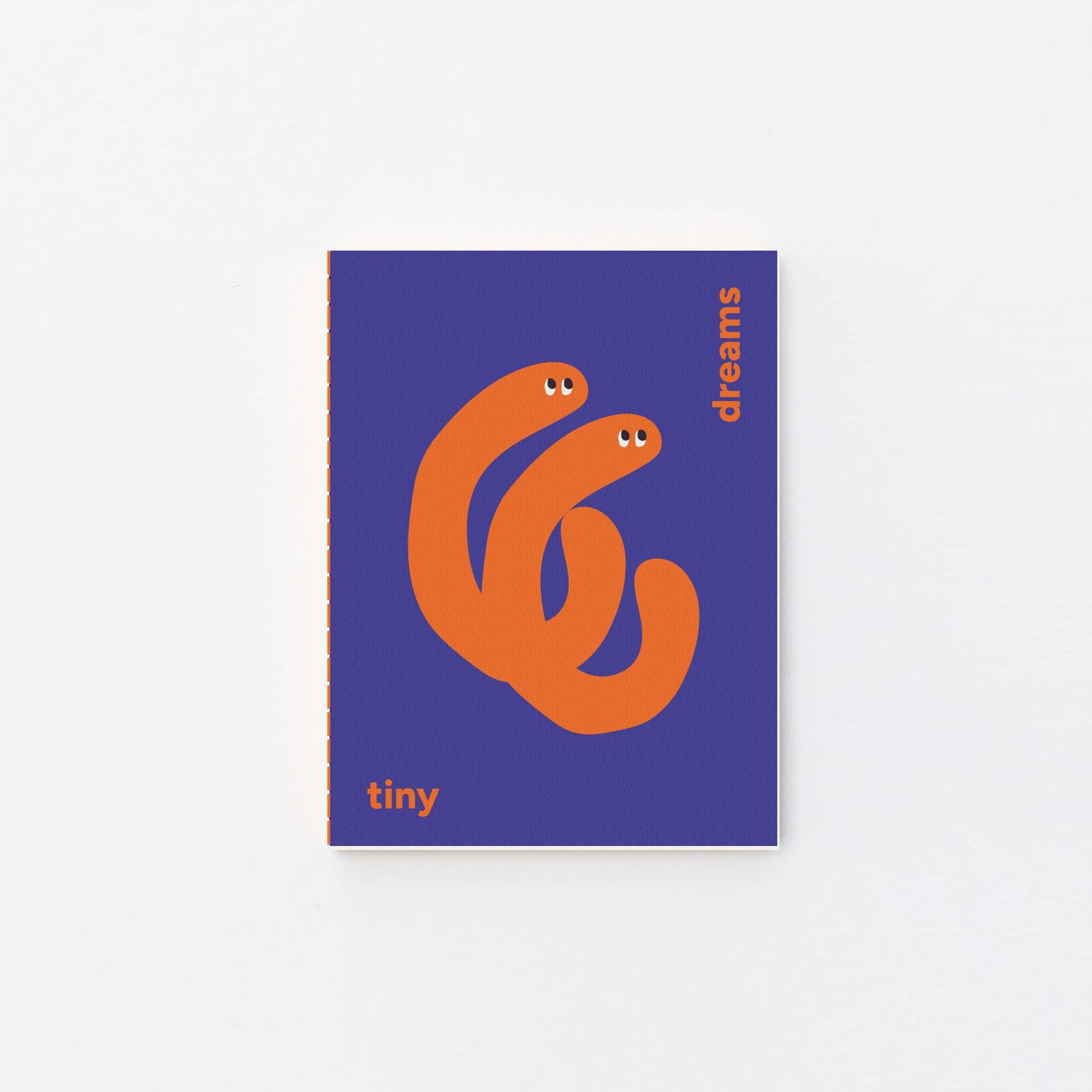A small notebook or book cover centered on a light gray background. The cover is purple with an orange abstract snake-like graphic and small orange text reading 'tiny' and 'dreams'.