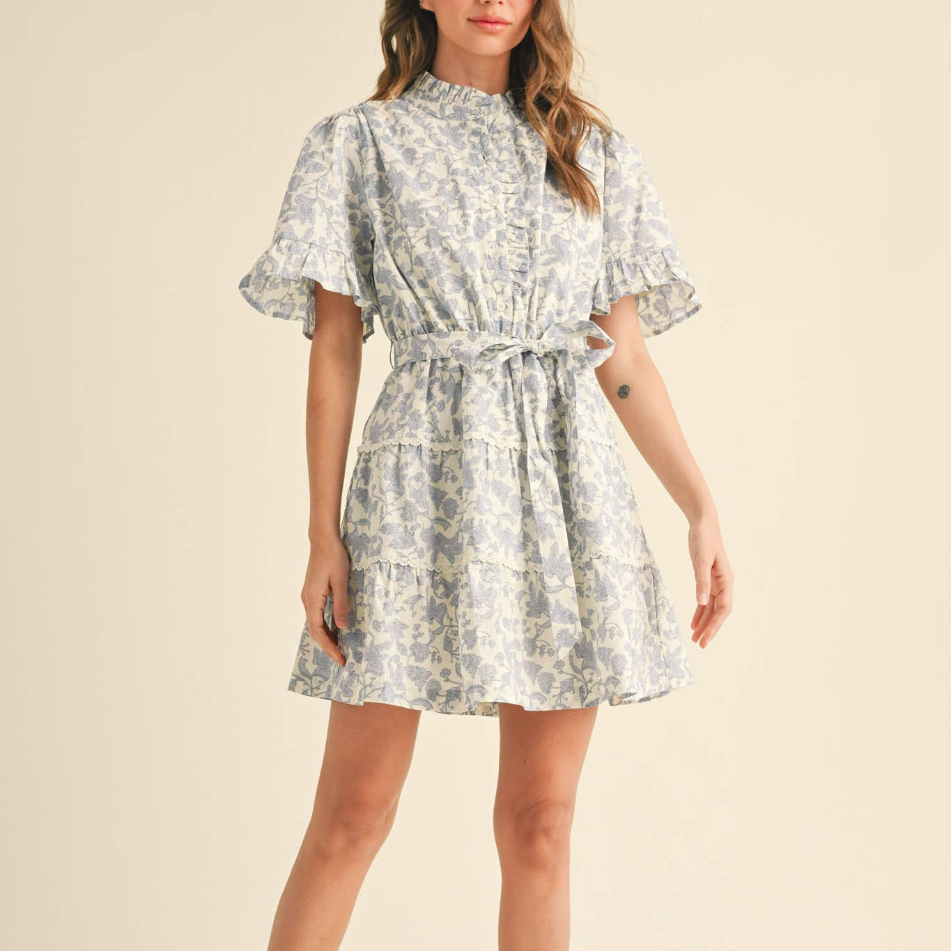Embrace your softest, most romantic style with this charming ruffled button-down floral mini dress. Every detail is designed to make you feel beautiful—from the delicate ruffled neckline and button placket to the sweet ruffle-trimmed short sleeves. The elastic waistband keeps you comfortable all day, while the self-tying belt lets you define your silhouette just how you like it. Tiered seams adorned with crochet lace add texture and movement, creating a look that feels both playful and put-together.