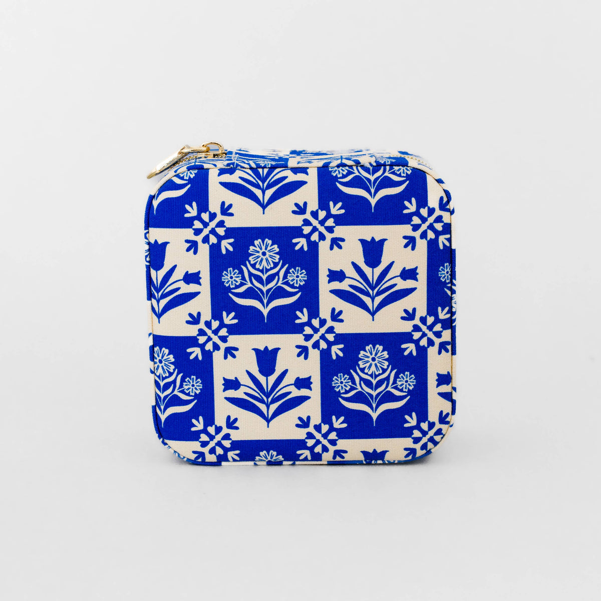 A small zippered pouch with a blue and white floral tile pattern, featuring a gold zipper pull, photographed on a light gray background.