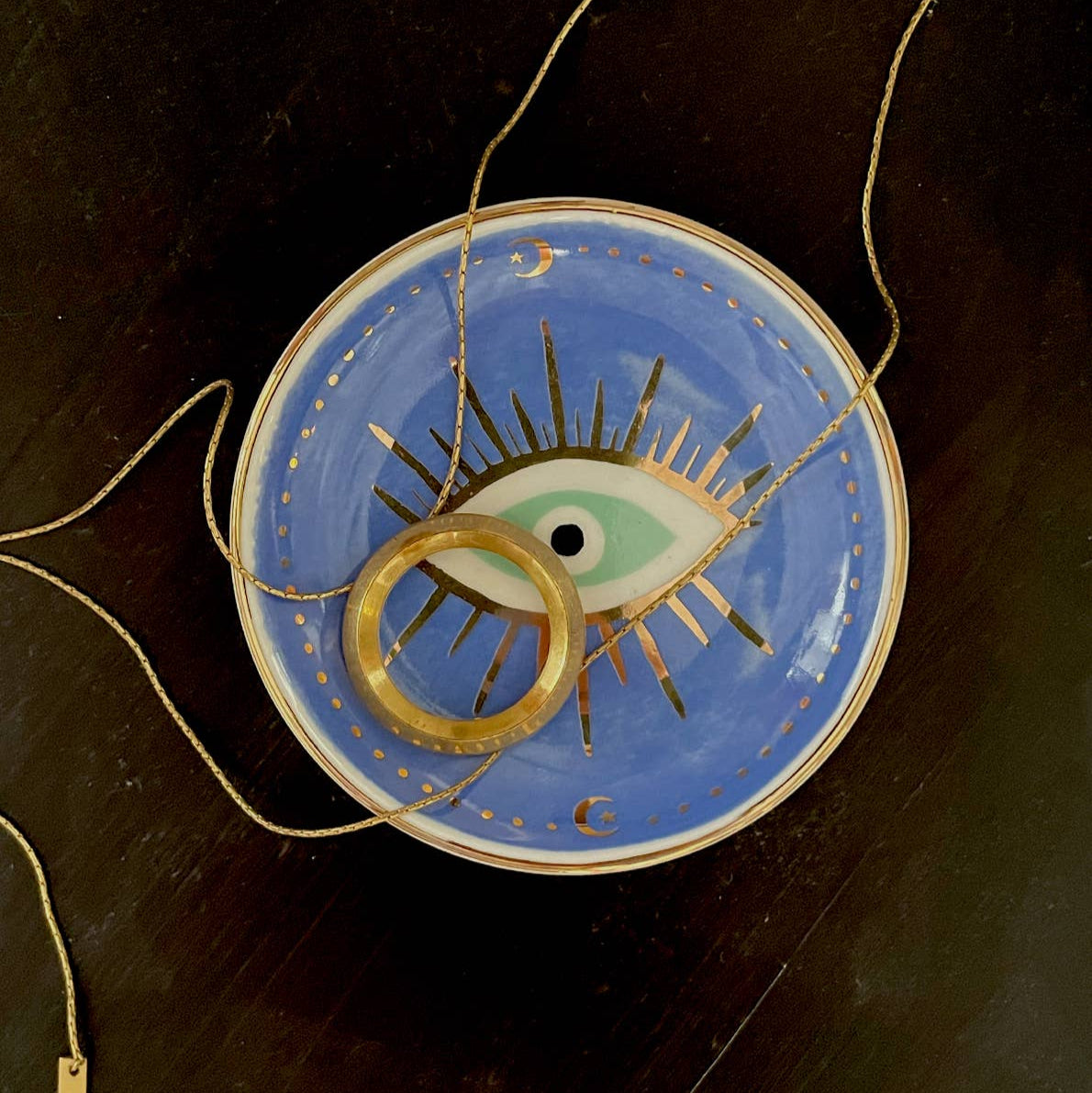 Decorative plate with eye design and gold ring on a dark surface
