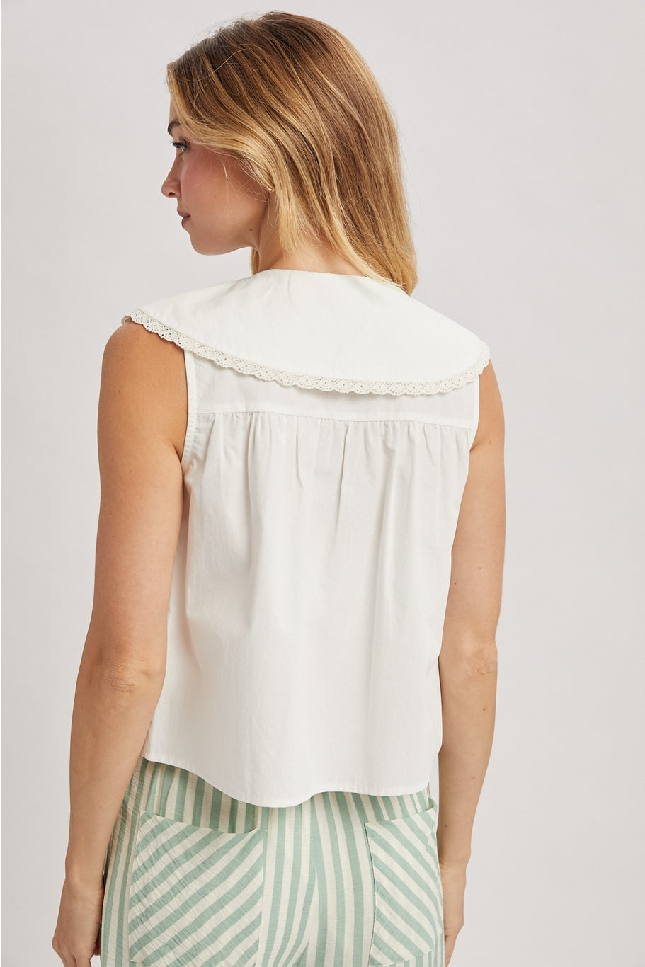 White sleeveless blouse with buttons and a large lace edged pan collar. 