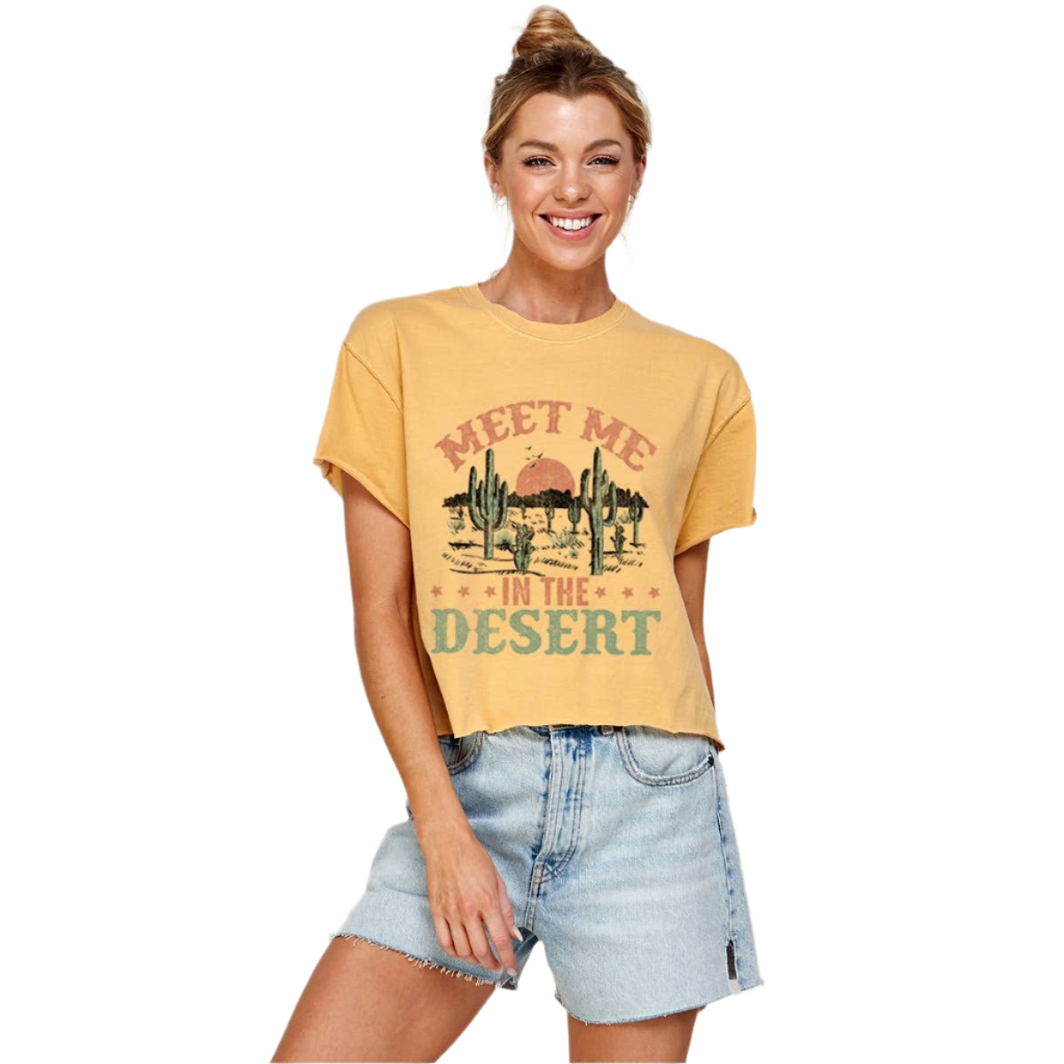Woman wearing a mustard yellow t-shirt with 'Meet Me in the Desert' graphic design on a plain background