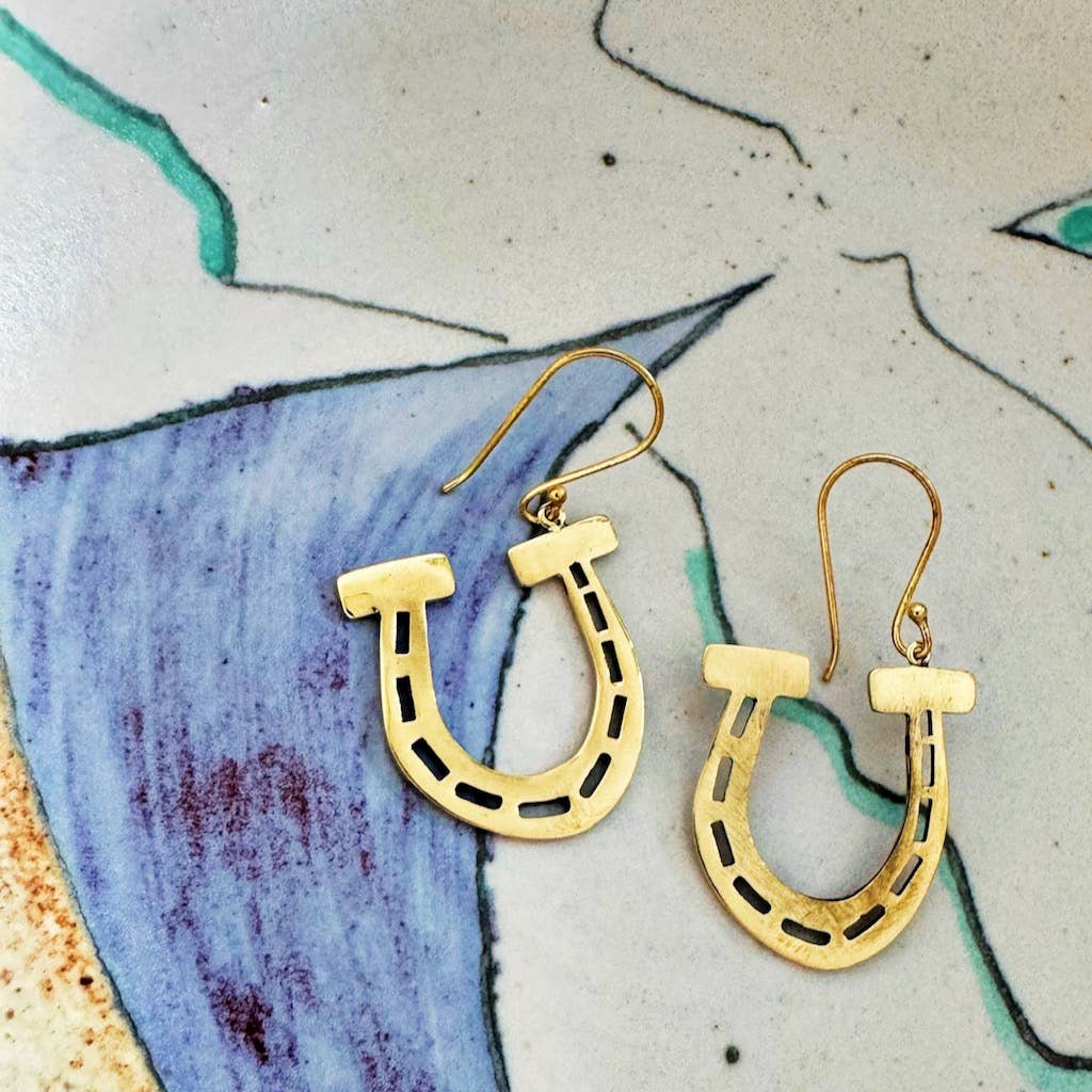 Gold horseshoe-shaped earrings on a textured surface with artistic design