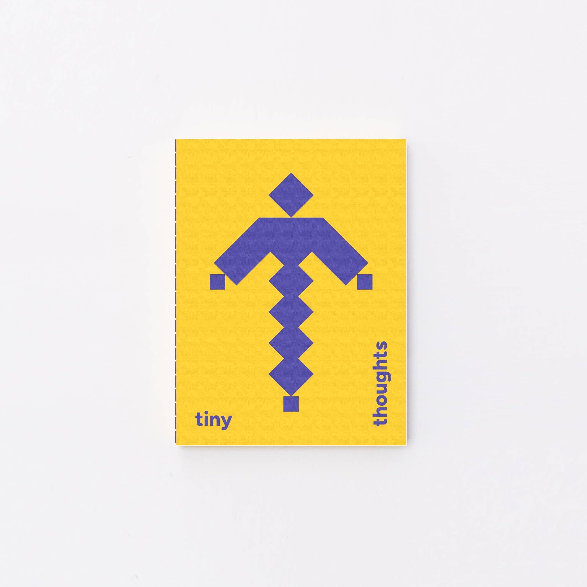 A small yellow tiny notebook with a purple geometric arrow graphic and the words 'tiny thoughts' printed on the cover, photographed against a plain white background.