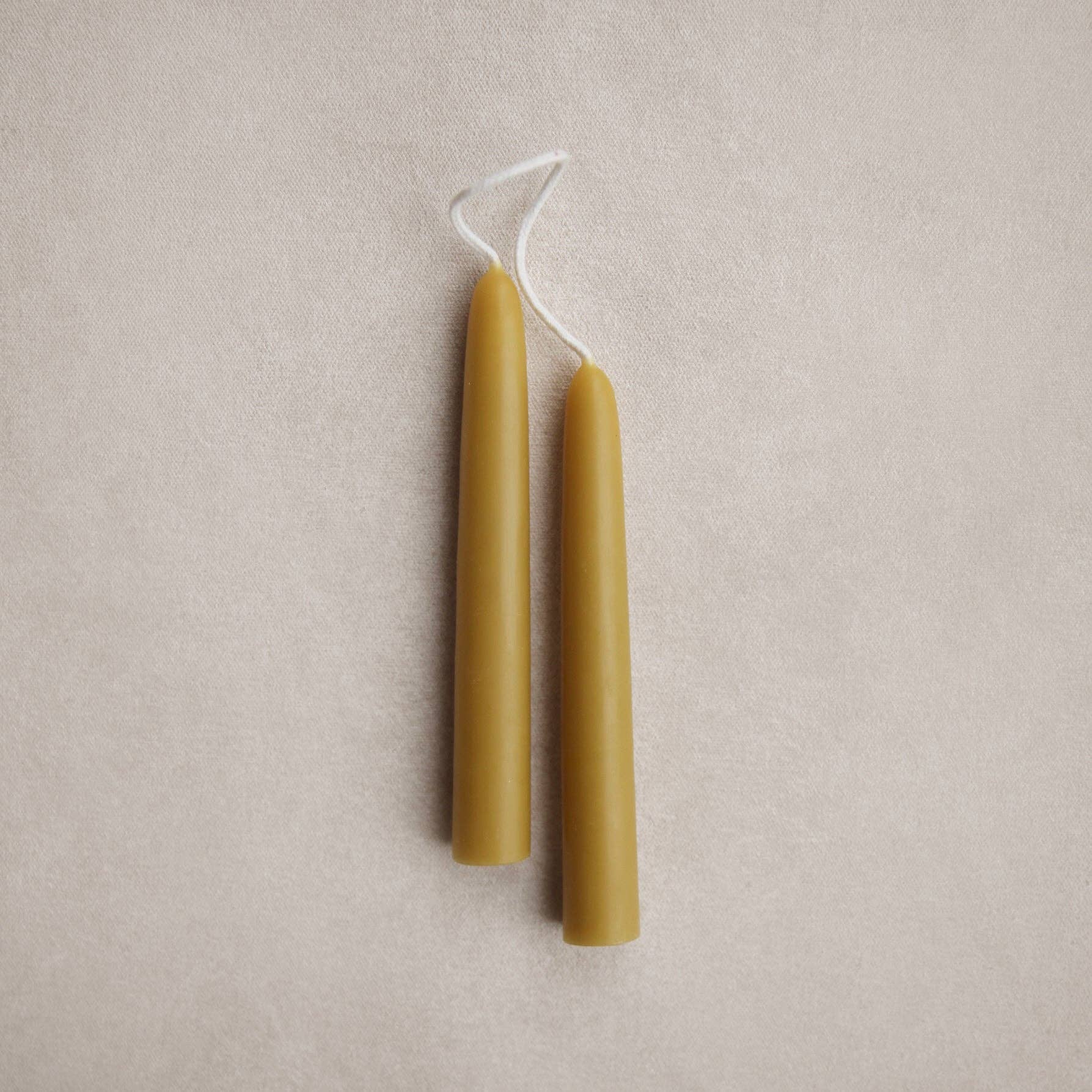 Two beeswax candles on a beige fabric background. Olive