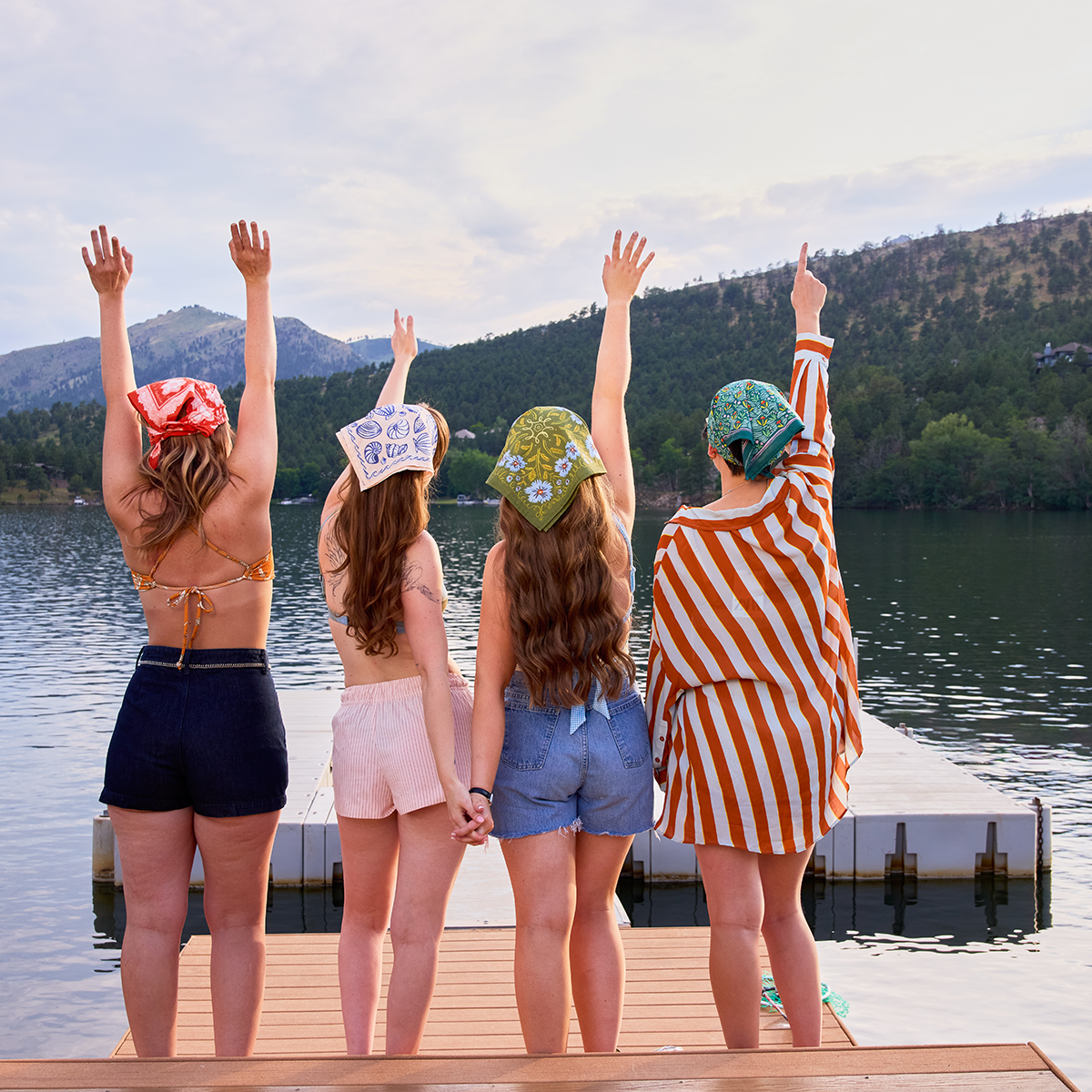 Four friends standing on a dock by a lake with mountains in the background
