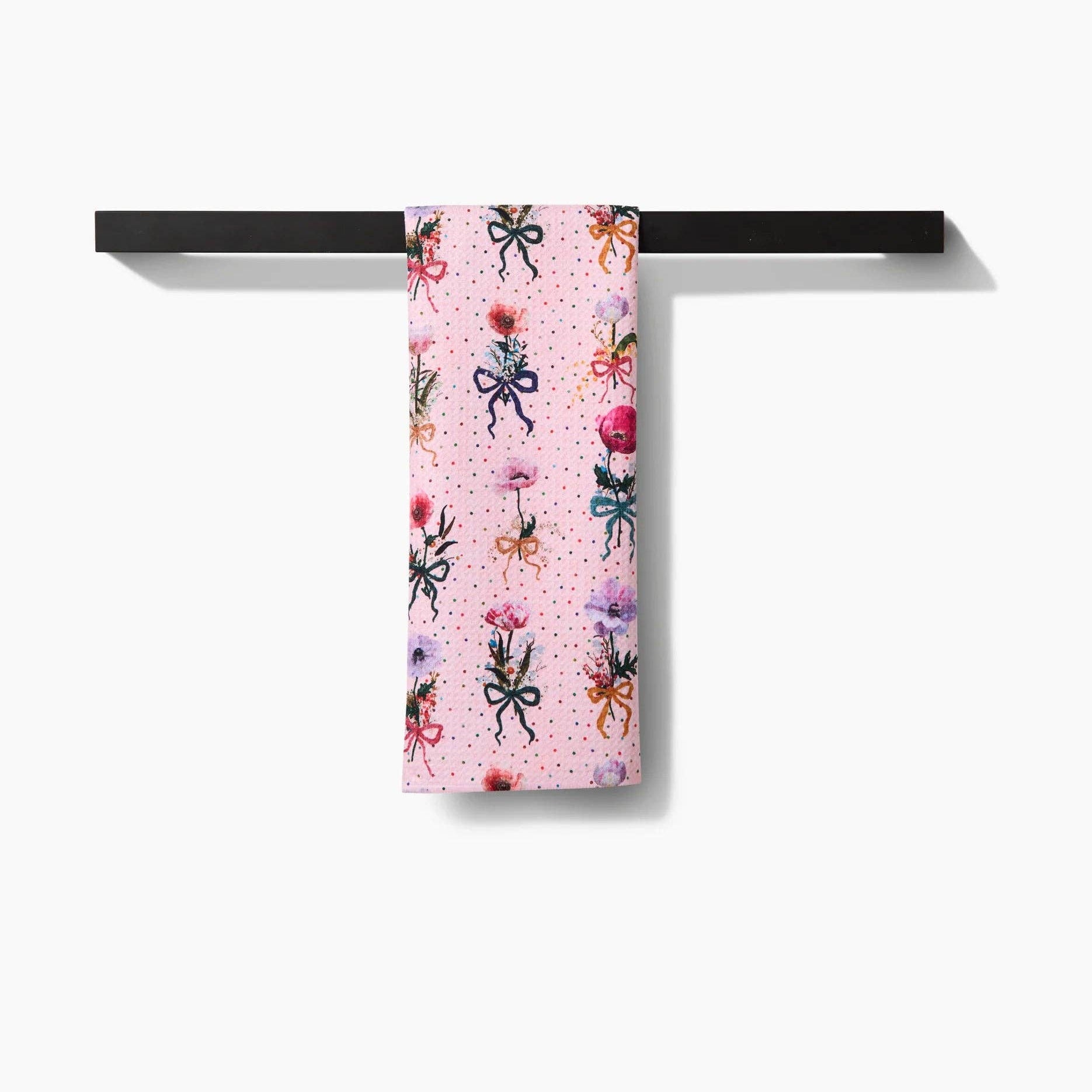 Decorative towel with floral and bow pattern hanging on a black rack against a white background Tea Towel
