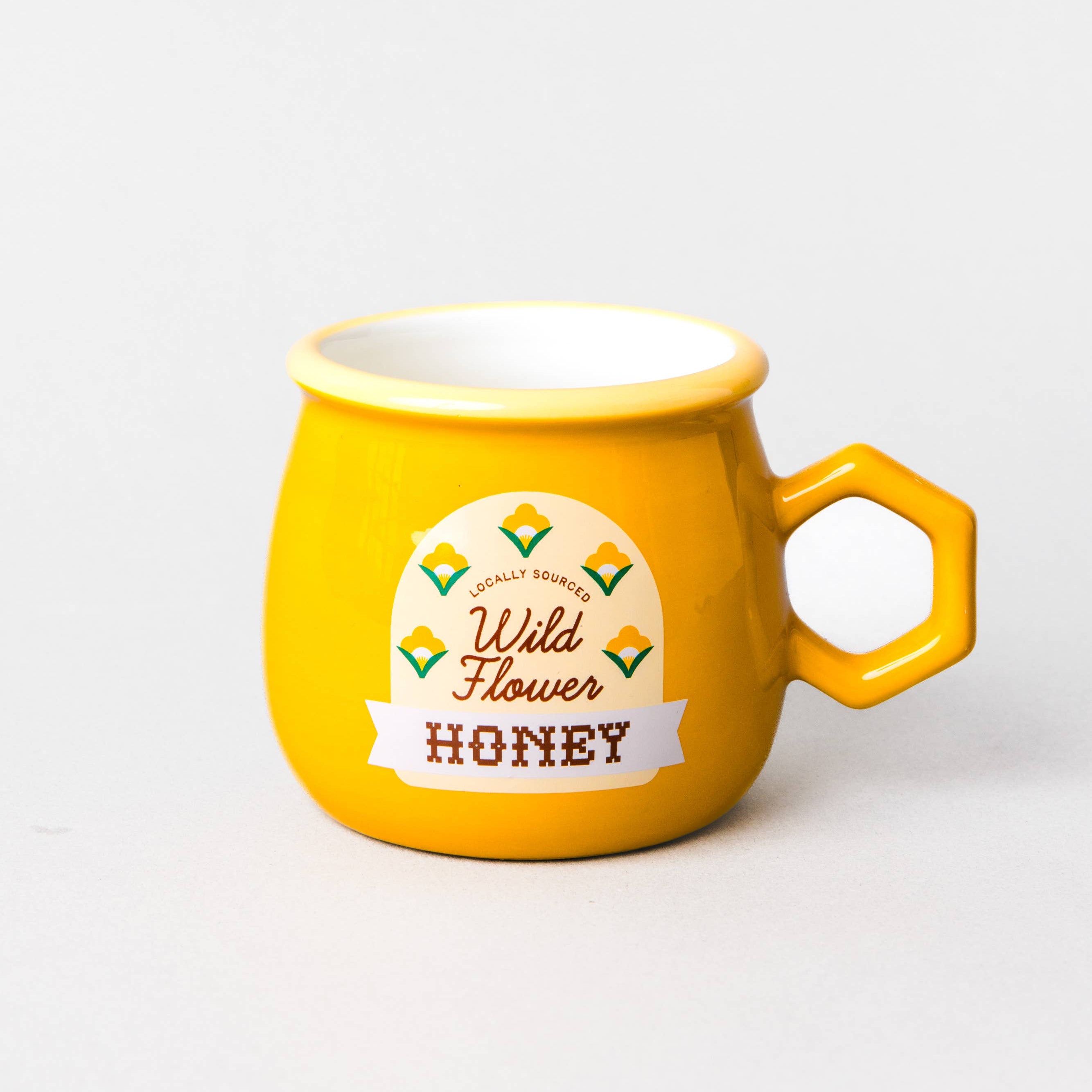 A bright yellow ceramic honey pot mug with a hexagonal handle, featuring a 'Wild Flower Honey' label on the front, set against a plain light gray background.