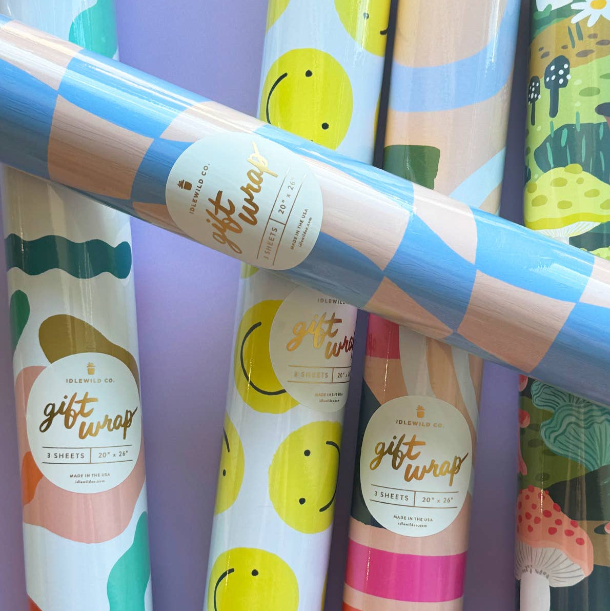 Rolls of colorful gift wrap paper with various designs on a purple background.