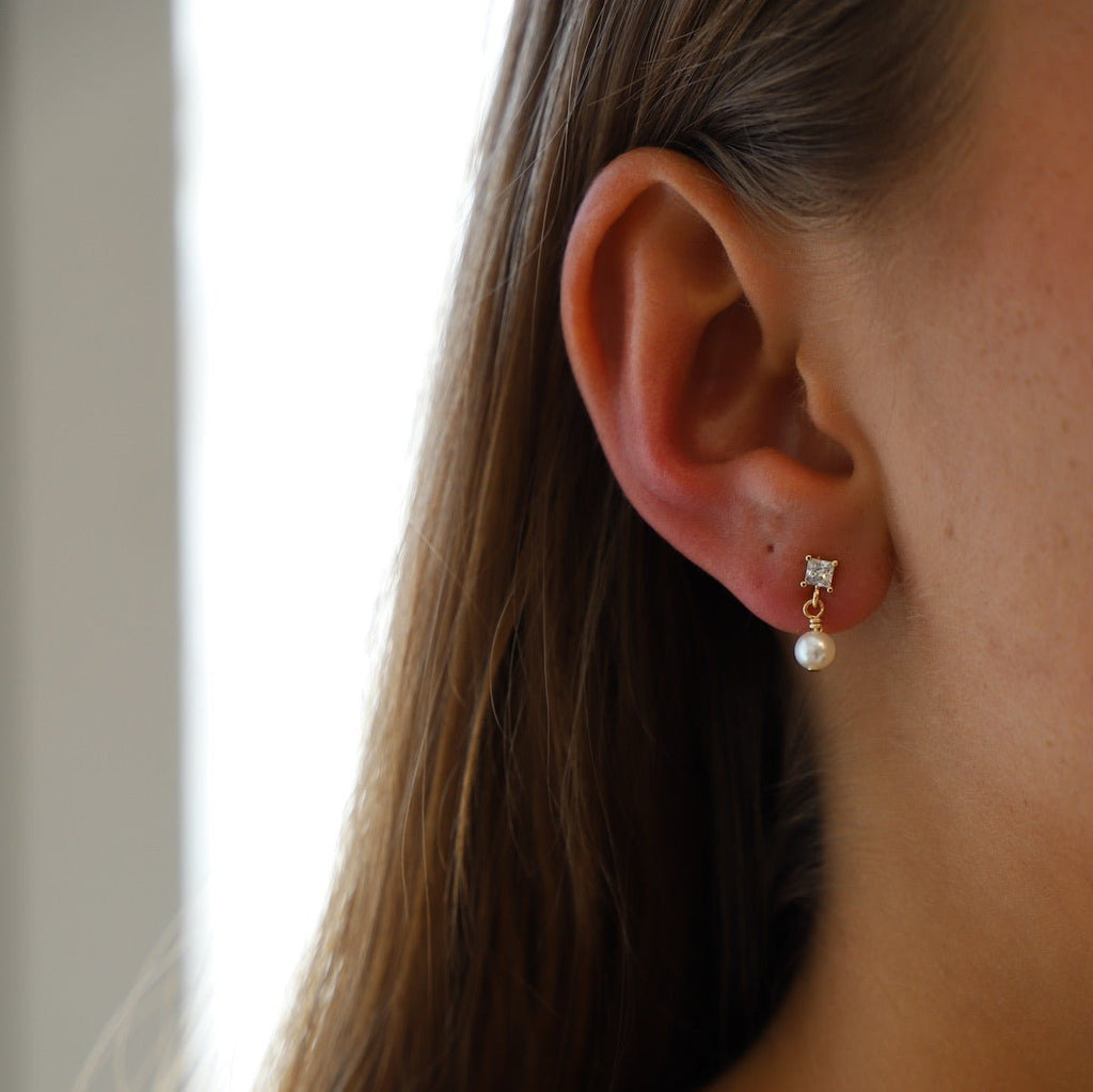 Add a touch of elegance with Claire Pearl Studs. These miniature cz square studs feature a freshwater pearl drop that will elevate any outfit. Perfect for those who love a hint of quirk and sophistication.