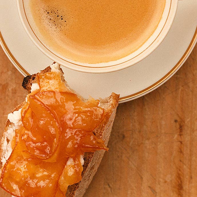 Toast with apricot jam and a cup of coffee on a wooden surface