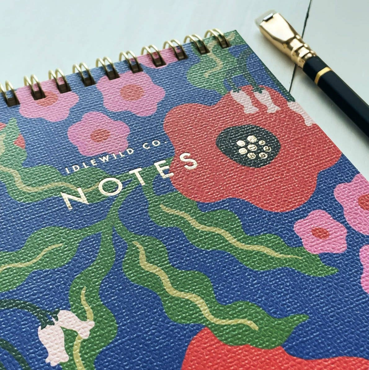 Floral notebook with 'Notes' text and a pen on a light blue background