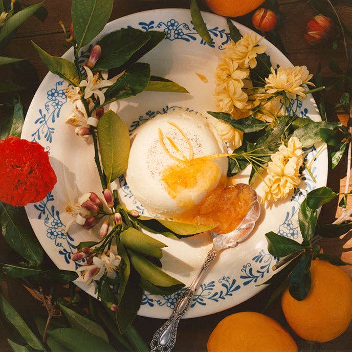 Scoop of ice cream with fruit on a decorative plate with flowers and oranges.