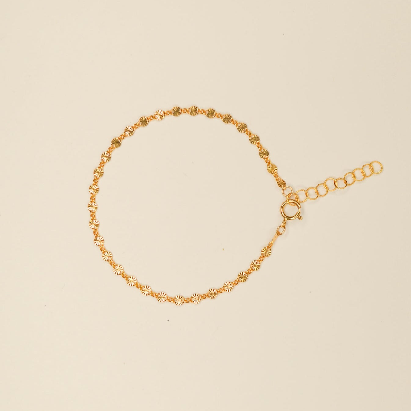 Delicate tiny flat ridged connecting disks make up this shimmery bracelet. Pictured on an off white background. 
