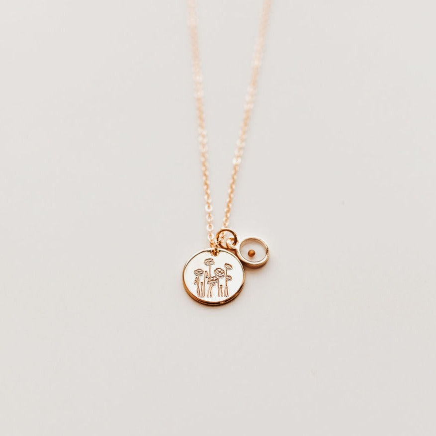 Gold circle pendant stamped with poppies, with an additional small glass locket with mustard seed inside, all strung on a simple gold chain.