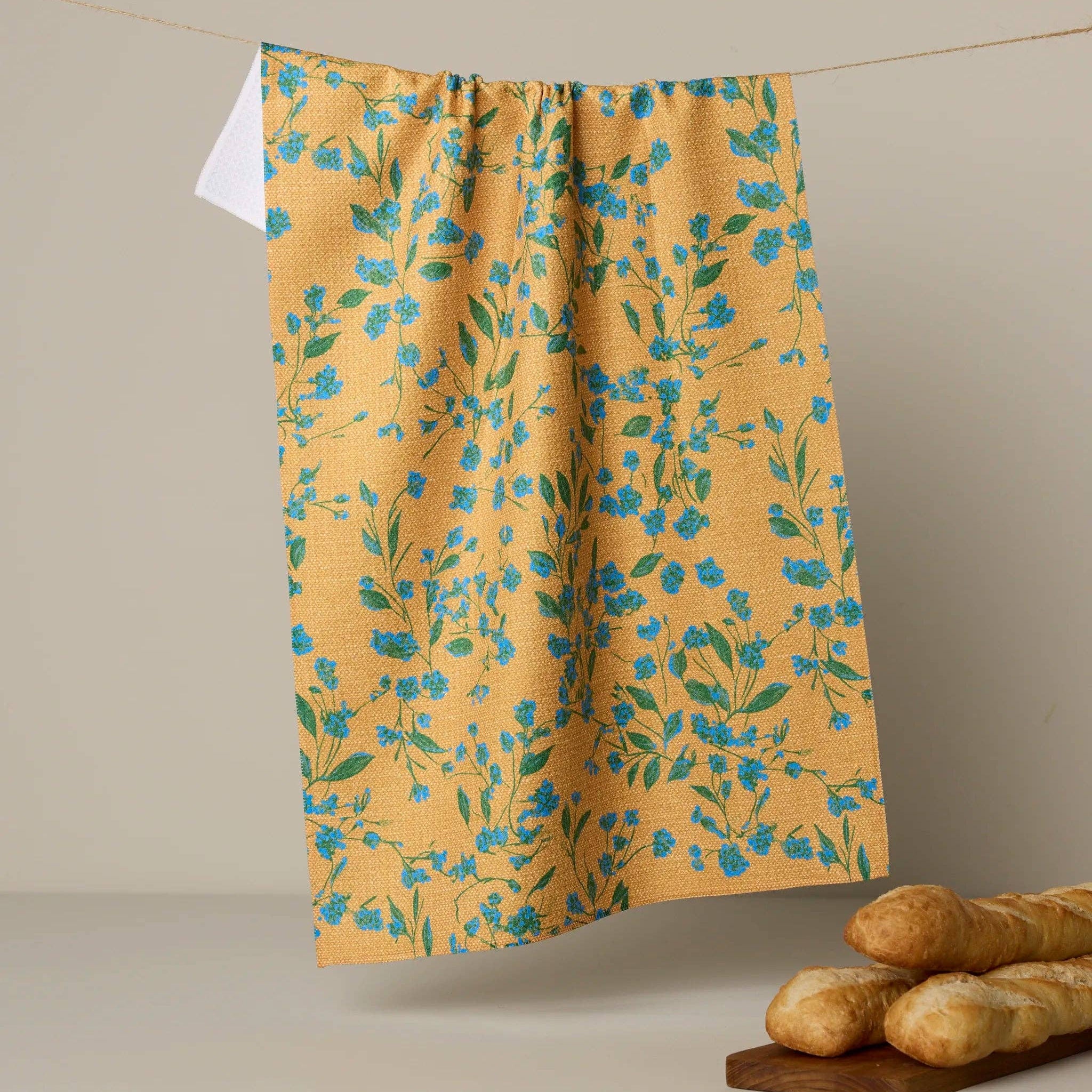 Yellow floral-patterned tea towel hanging on a line with bread on a wooden board below.