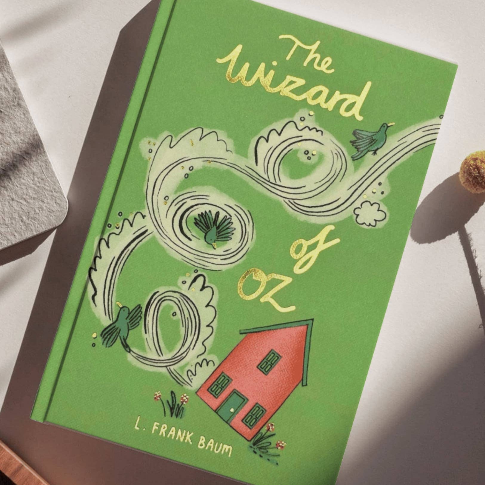 Green book cover of 'The Wizard of Oz' by L. Frank Baum on a white surface.