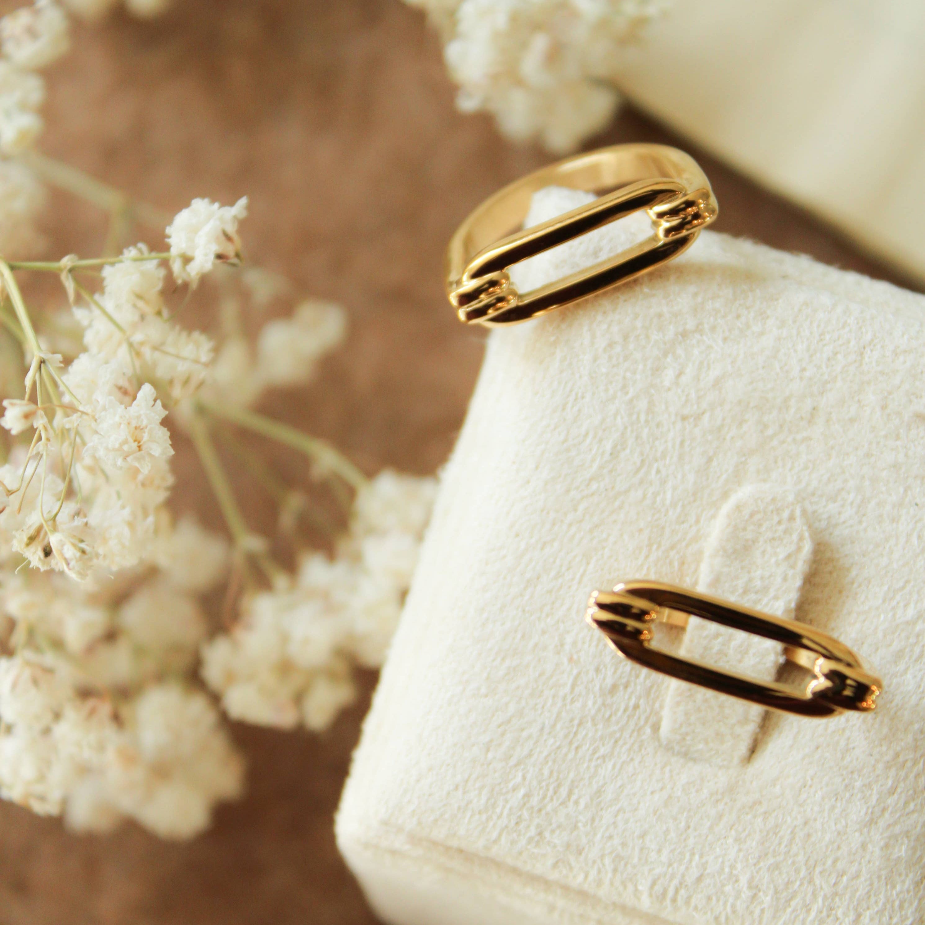 Gold ring on a textured white surface with white flowers in the background