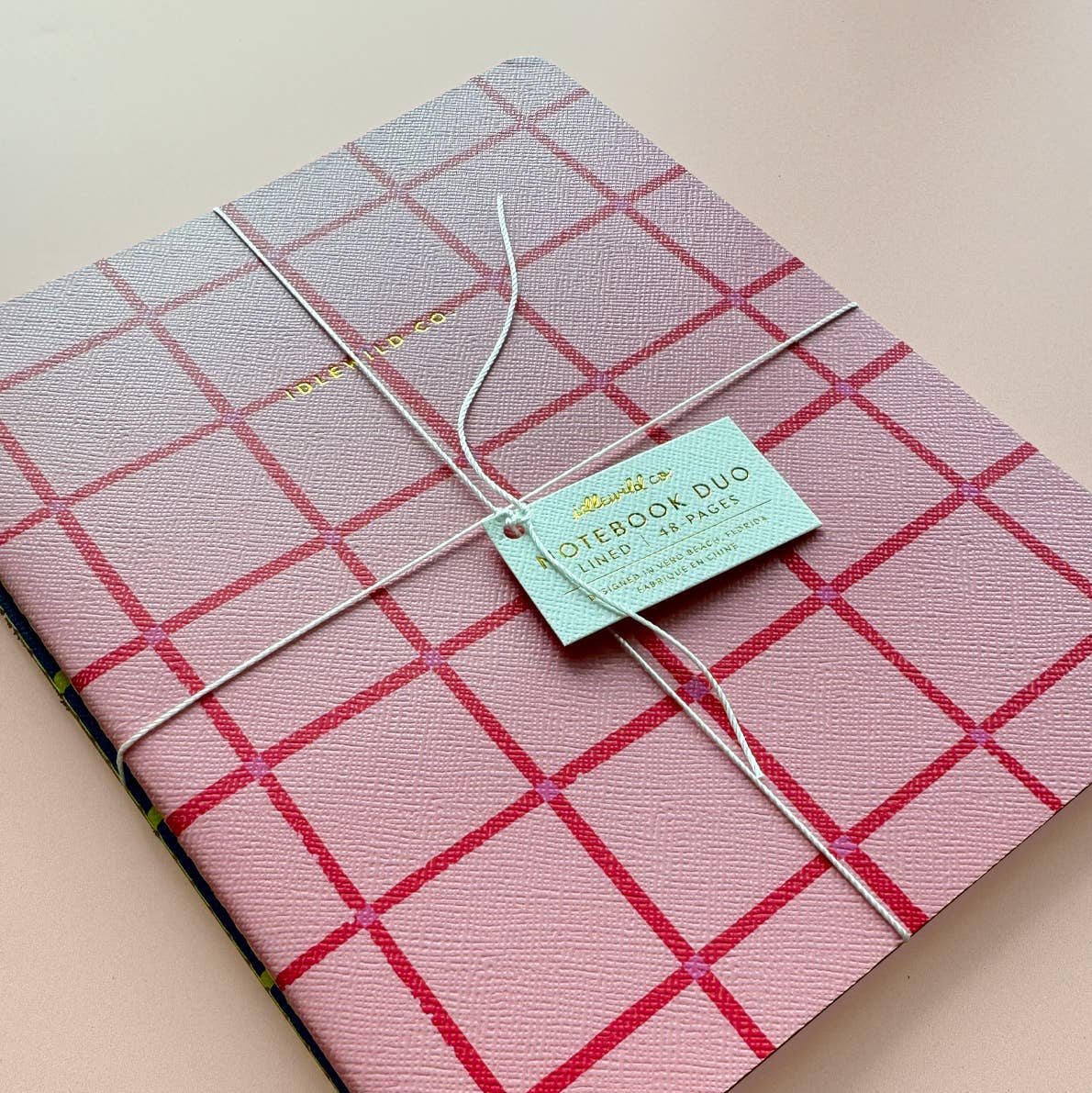 Pink checkered notebook with a green tag on a beige background