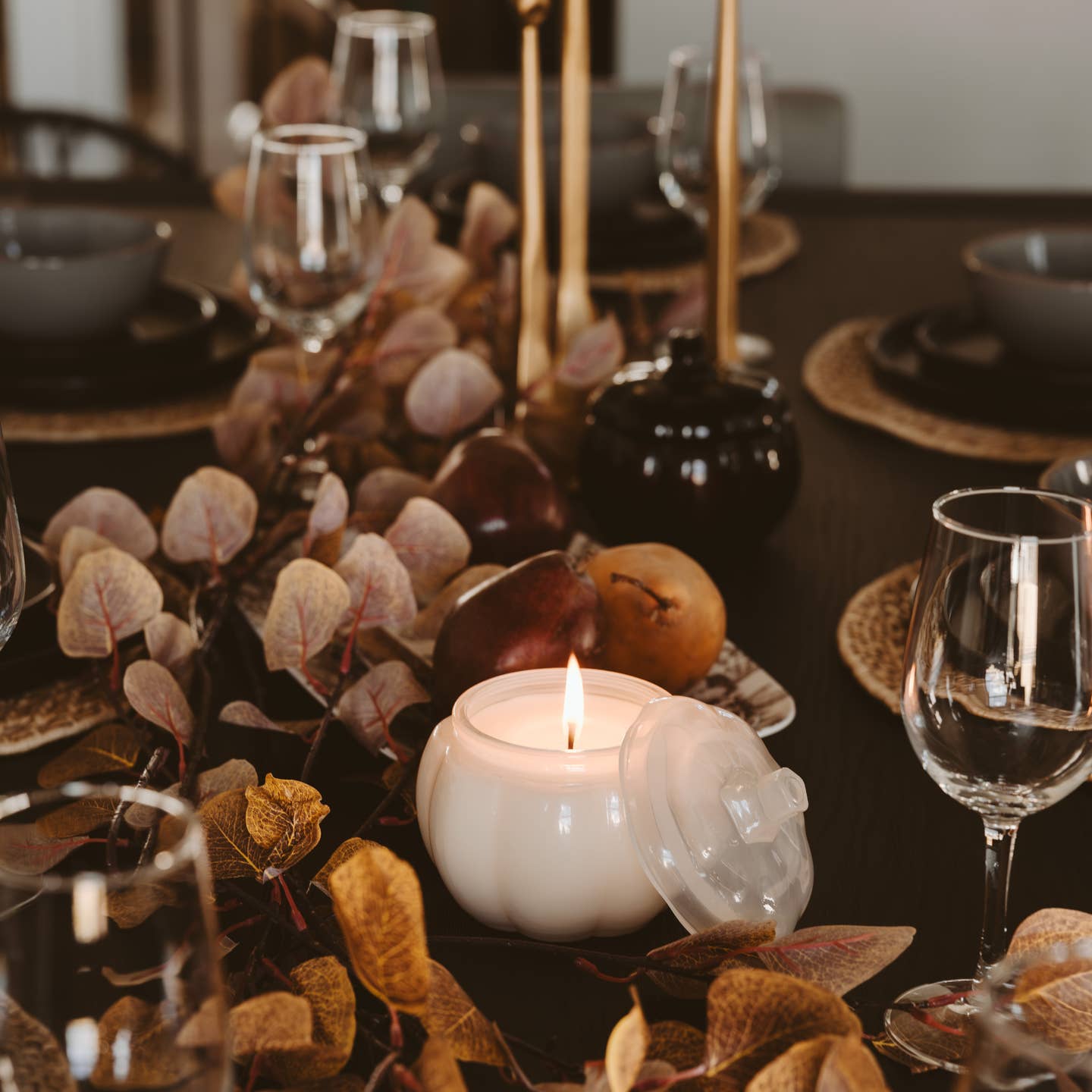 Decorative table setting with candles, glasses, and leaves on a dark surface