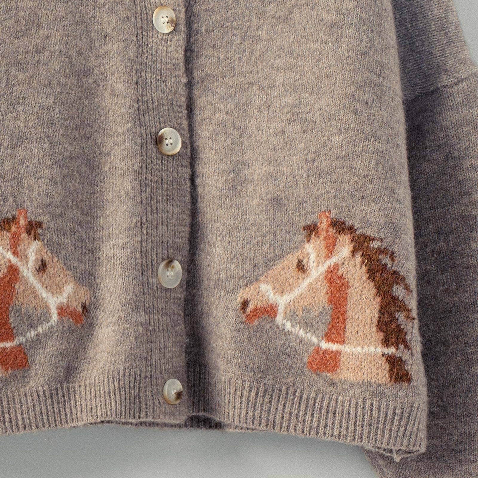 Mocha knitted cardigan with horse designs on a hanger against a light background