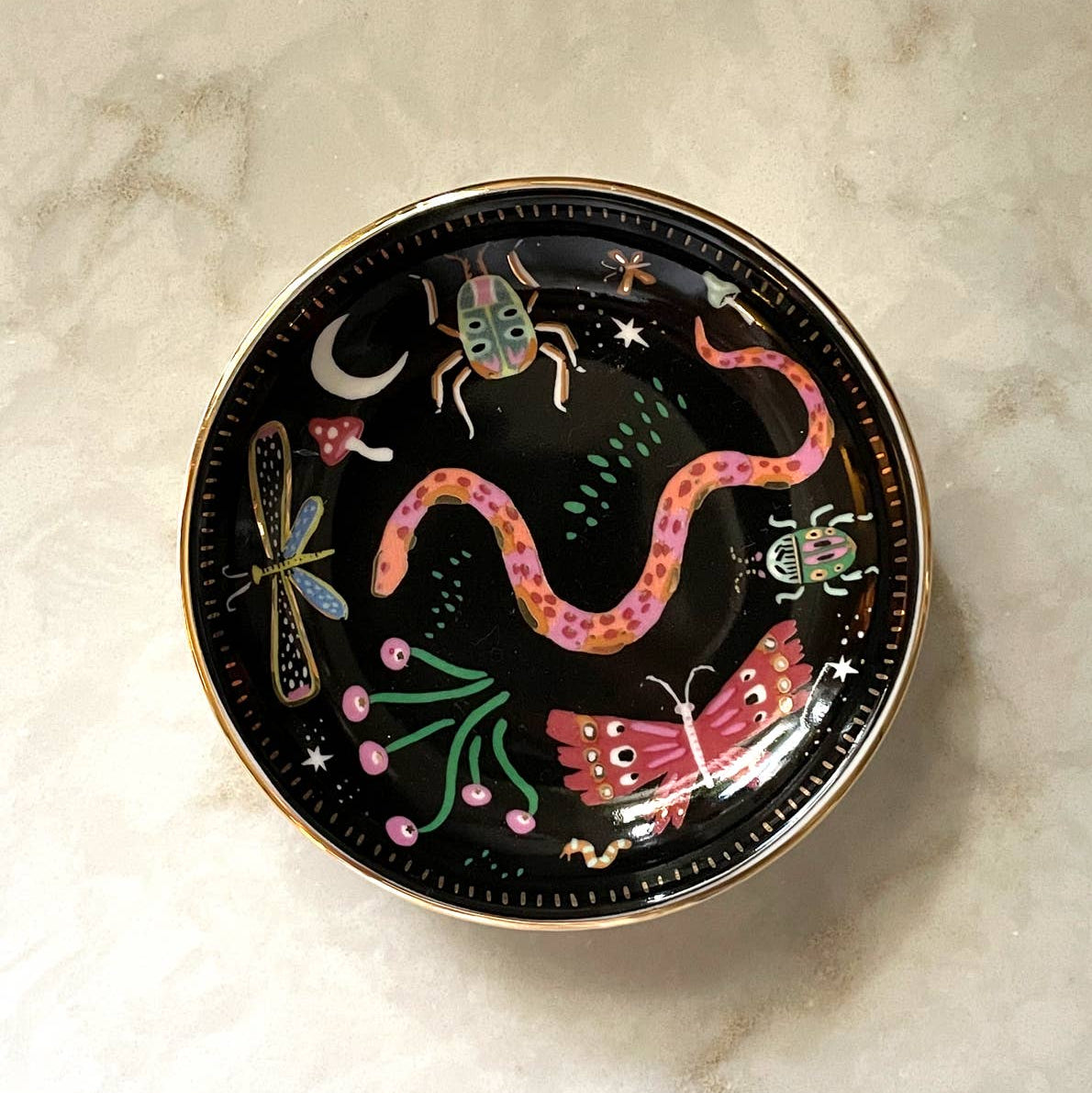 Decorative plate with colorful insect designs on a marble surface