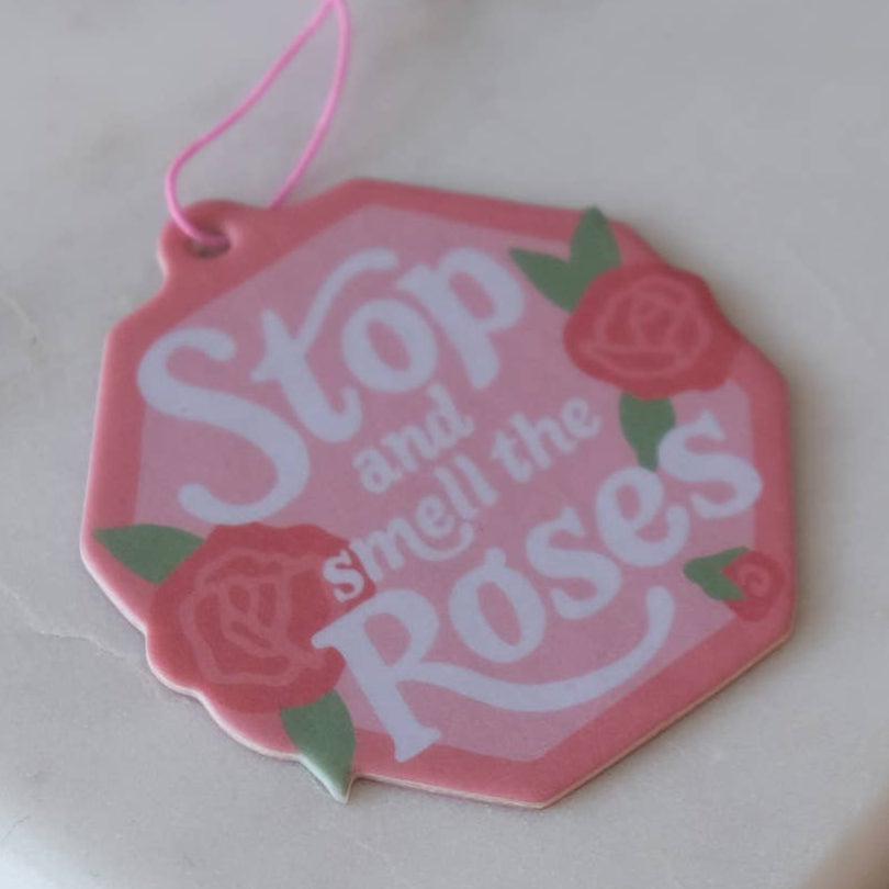 Pink hexagonal air freshener with 'Stop and smell the Roses' text and roses on a white background