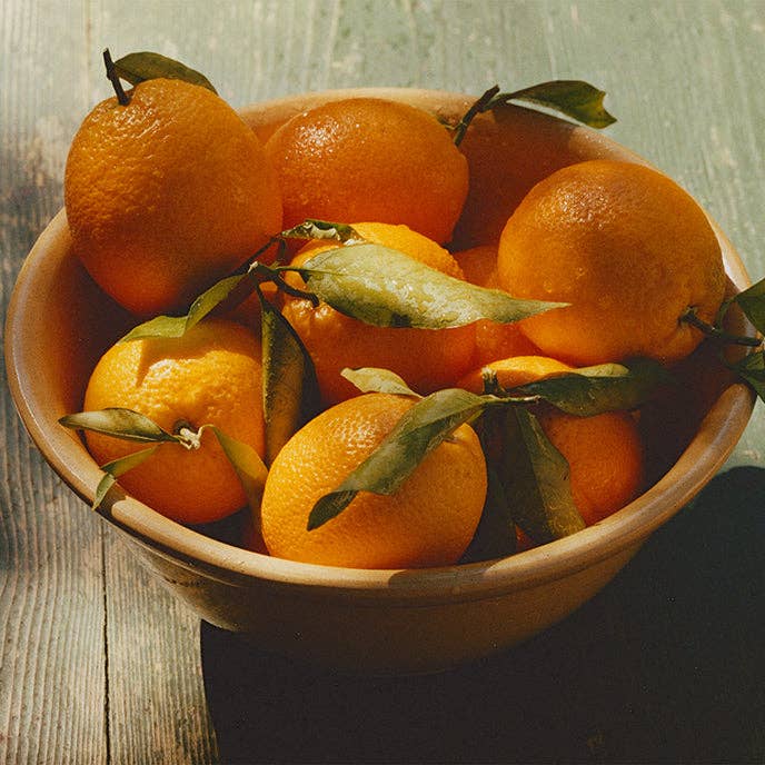 Bowl of oranges with leaves on a wooden surface