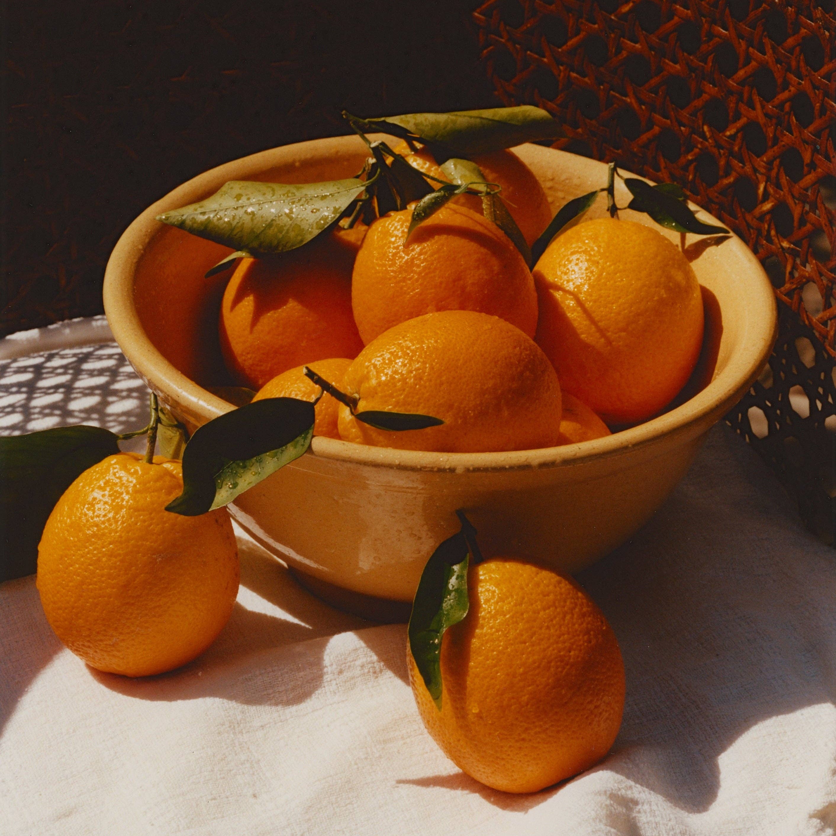 Bowl of oranges with leaves on a textured surface