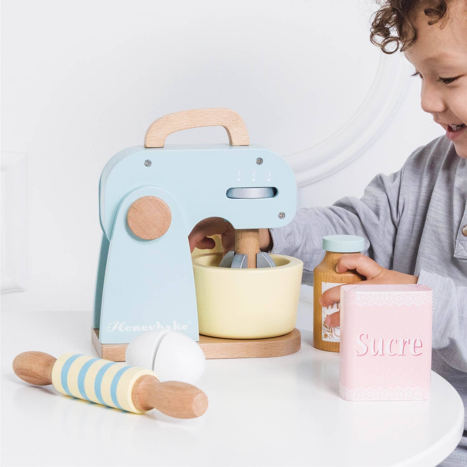 Child playing with a set of colorful kitchen toys on a white surface.