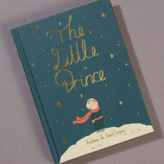 Book titled 'The Little Prince' with a blue cover and gold text on a gray background