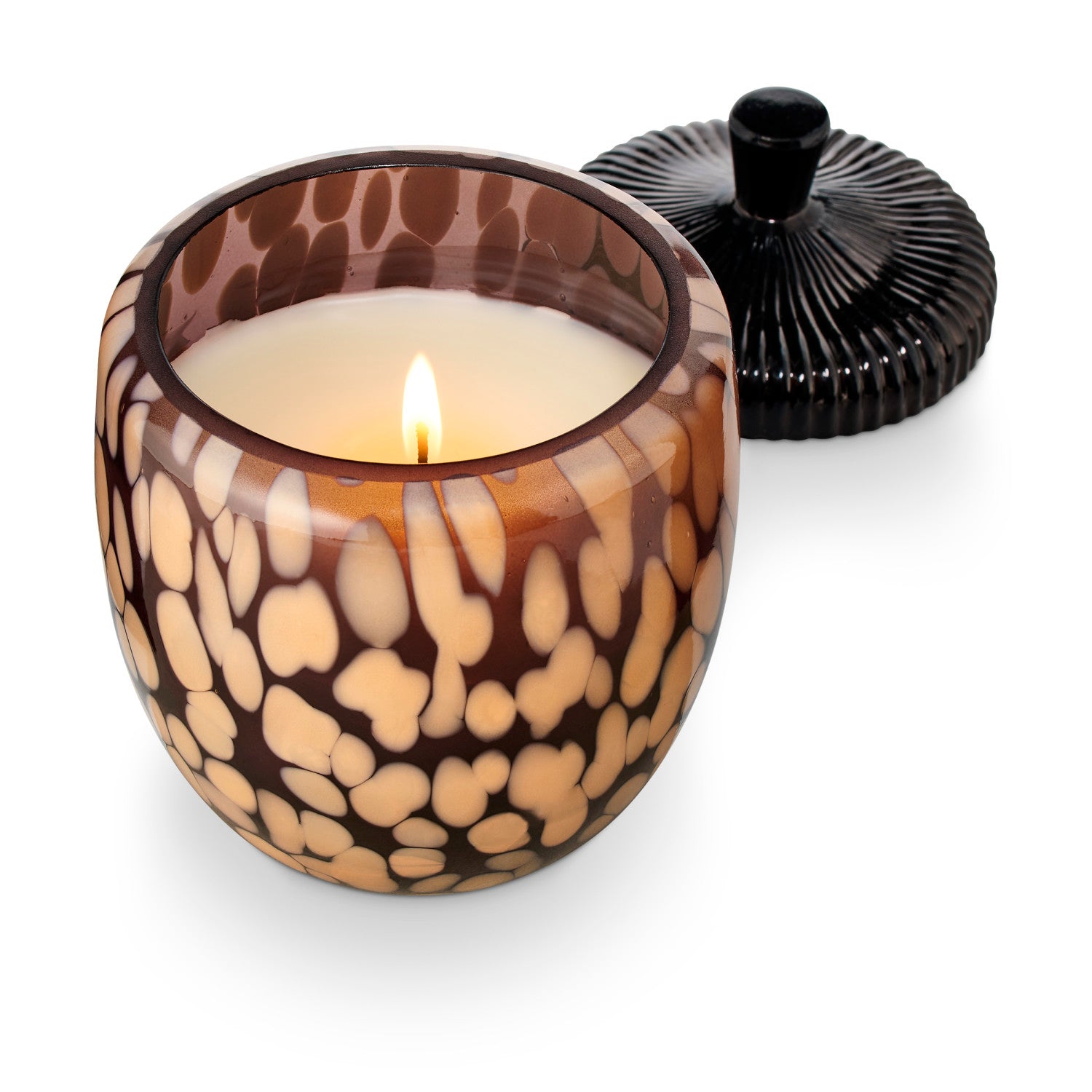 Candle in a patterned glass holder with a black lid on a white background