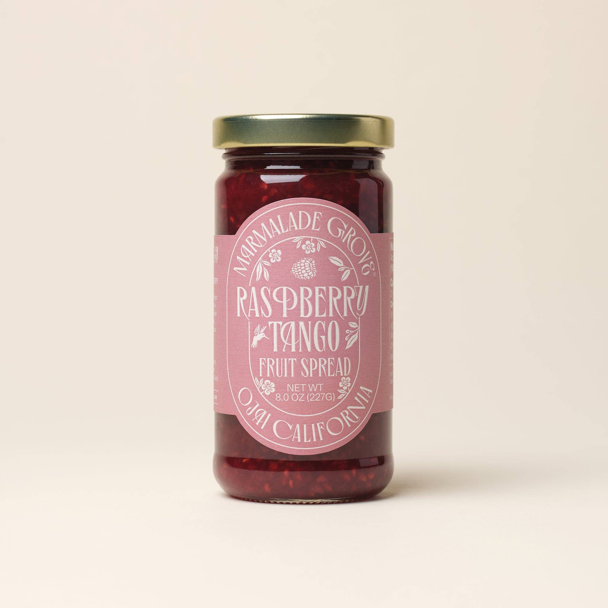 A glass jar of Normalade Gourmet Raspberry Tango Fruit Spread with a pink label and gold lid, centered on a light beige background.
