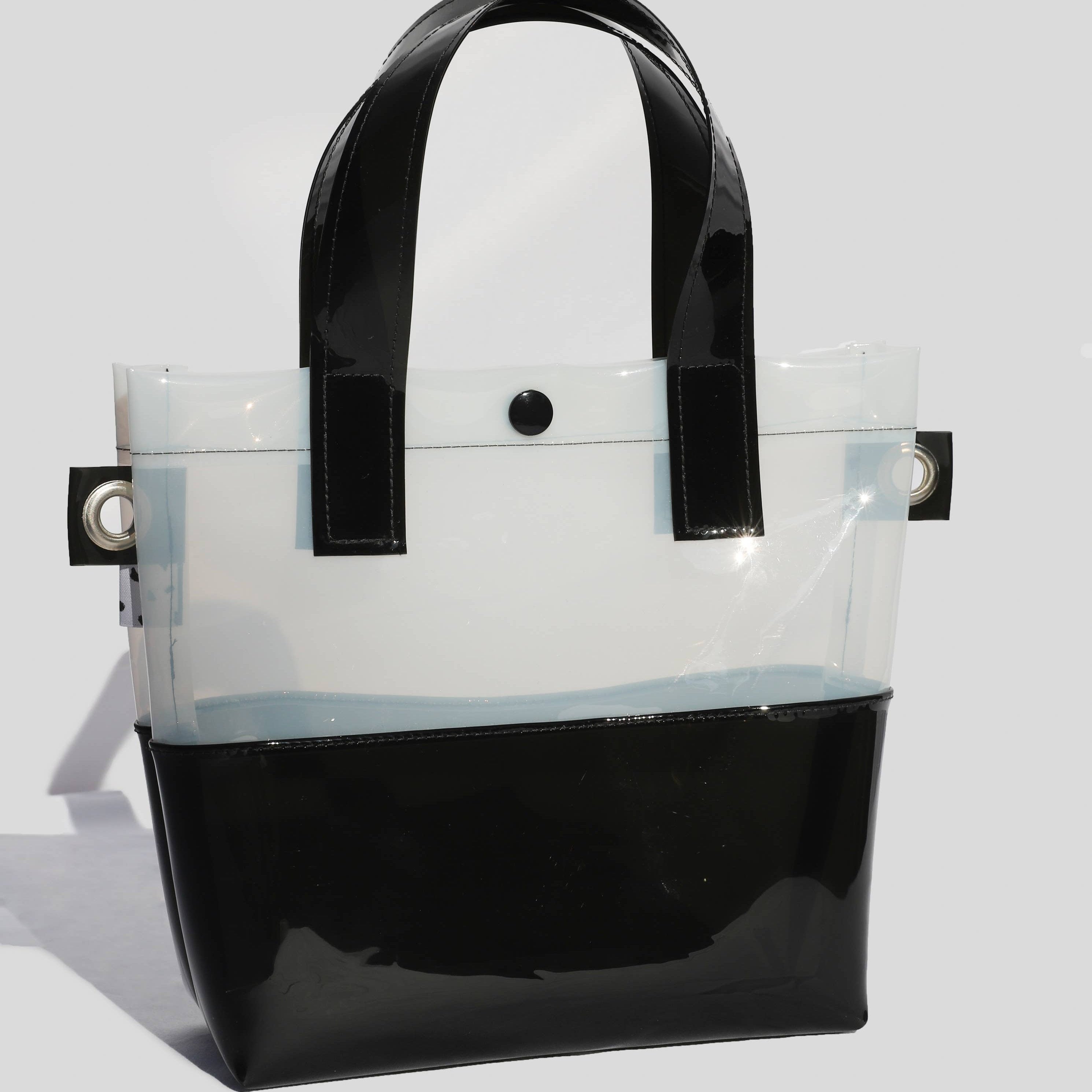 Miss your jelly sandals? This is your new favorite bag! Keep everything inside with a snap. The black and white translucent vinyl handle bag has a black snap closure and is detailed with silver metal grommets. It's available with or without the detachable black and white checkered 1" strap