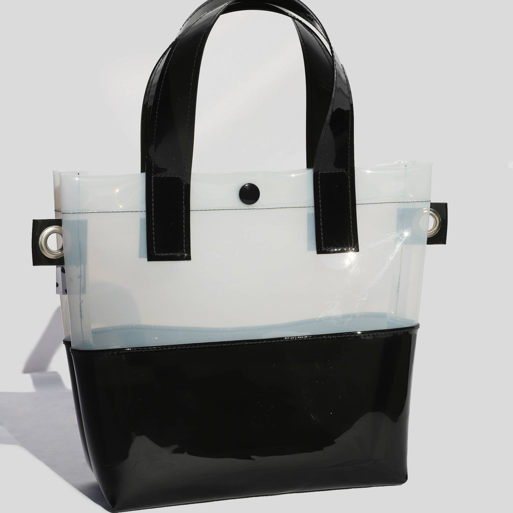 Miss your jelly sandals? This is your new favorite bag! Keep everything inside with a snap. The black and white translucent vinyl handle bag has a black snap closure and is detailed with silver metal grommets. It's available with or without the detachable black and white checkered 1" strap