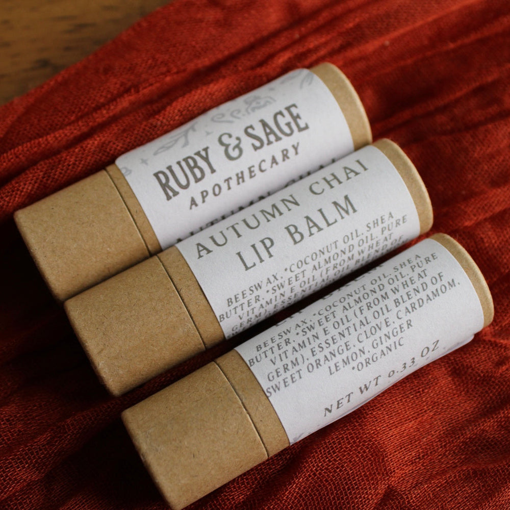 Autumn Chai Lip balms with neutral packaging against a rust colored table runner.
