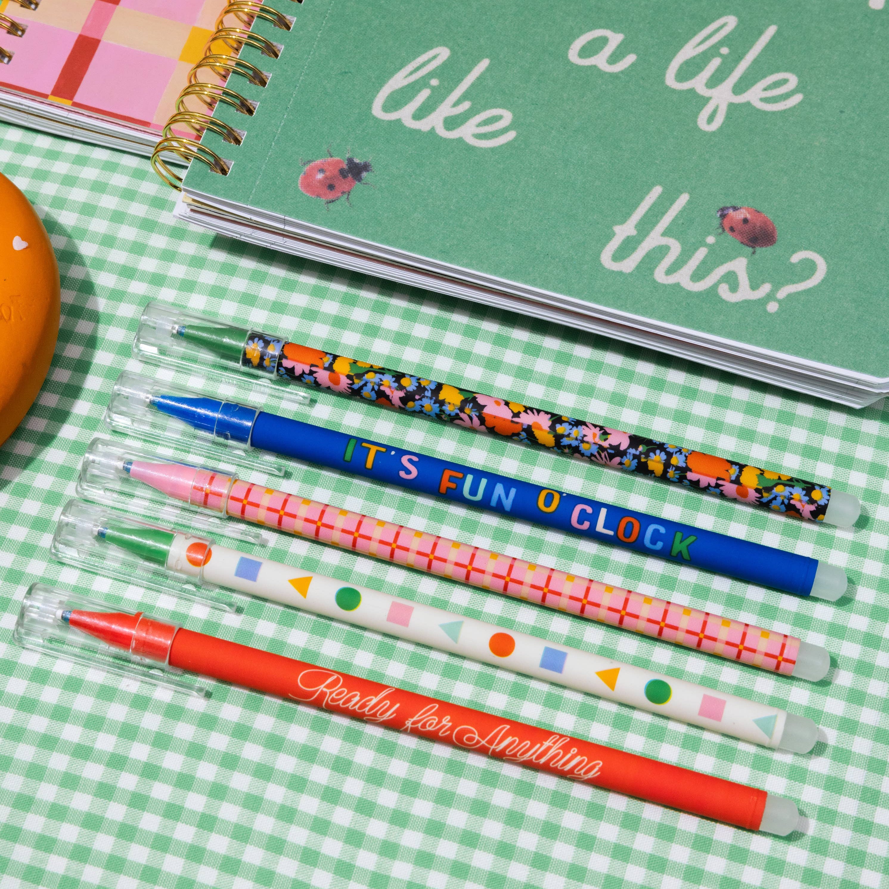 Colorful pens and a green notebook with text on a checkered tablecloth